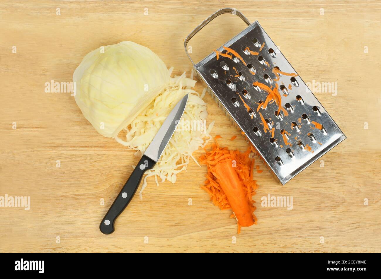 Krautsalat Zutaten, Weißkohl und Karotte auf einem Schneidebrett mit einem Messer und einer Reibe Stockfoto