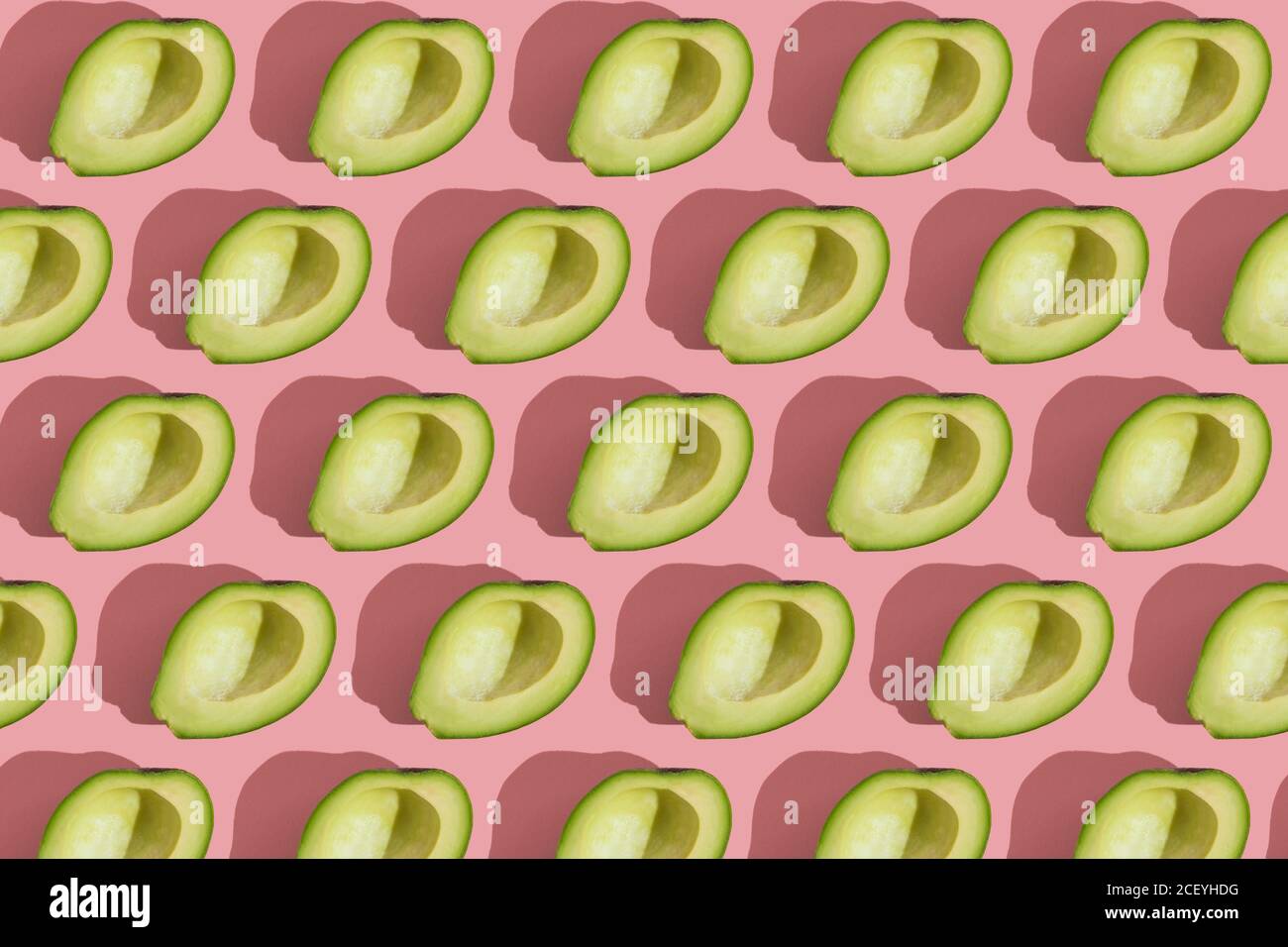 Trending Stil Muster der Hälfte seedless grün Avocado auf rosa Hintergrund mit hartem Licht. Kreative Lebensmitteltextur Stockfoto