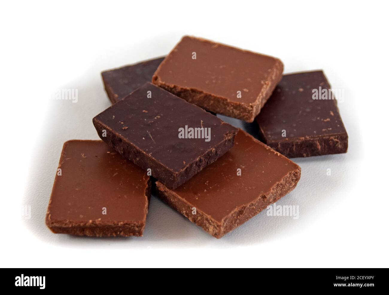 Milch- und dunkle Schokoladenwürfel. Schokoladenstapel auf weißem Hintergrund. Stapel Schokolade. Kleine dunkle Schokoladenstücke. Stockfoto