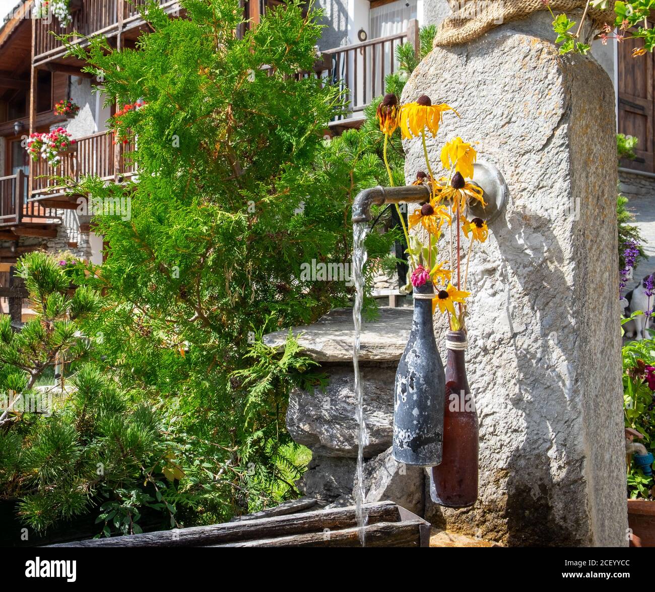 Alte Brunnen und Flaschen mit gelben Blumen in dem kleinen Dorf von Usseaux, Piemonte, Italien Stockfoto
