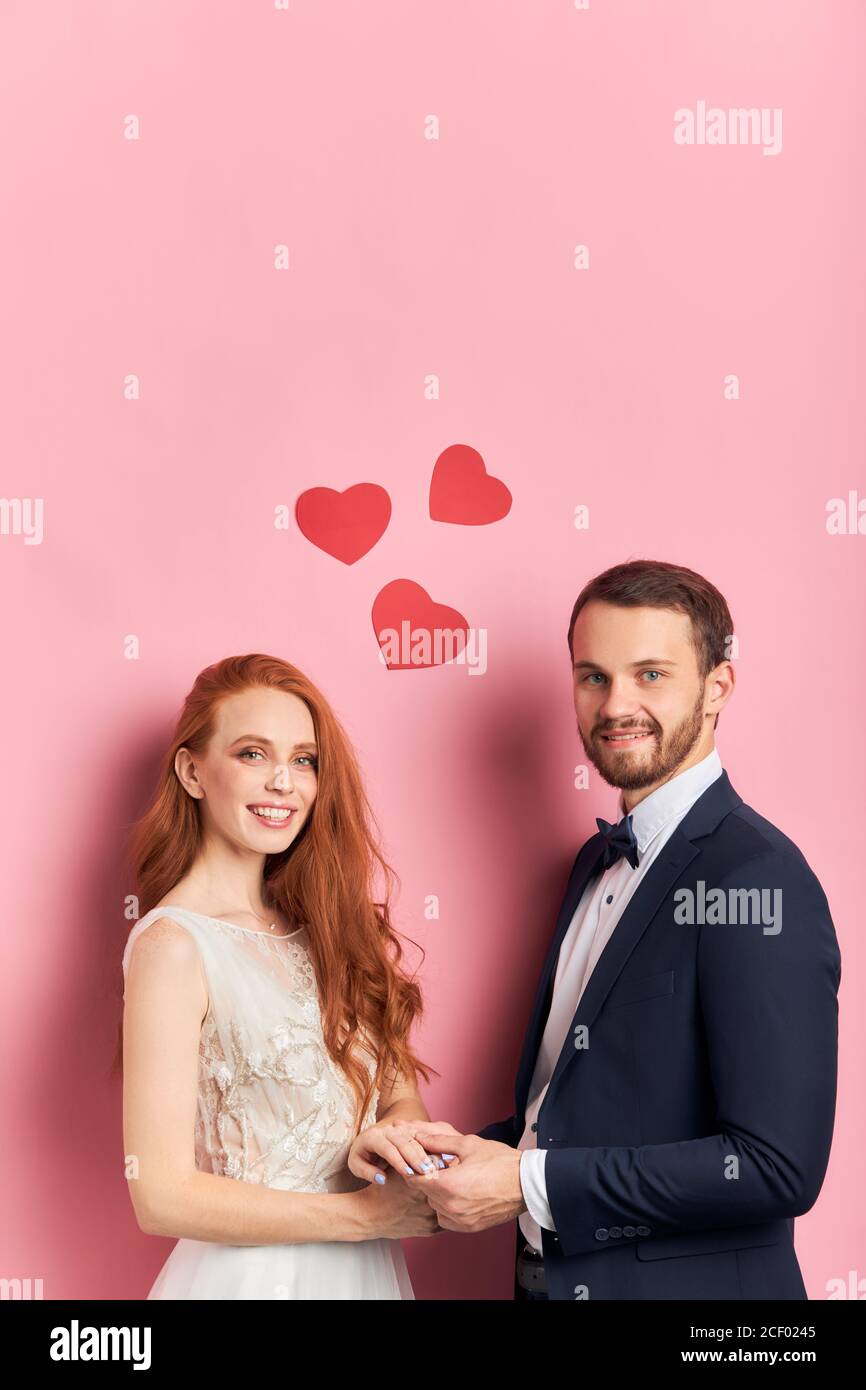 Nettes junges Paar frisch verheiratet isoliert über rosa Hintergrund. Attraktive junge Menschen in Liebe zusammen. Hochformat Stockfoto