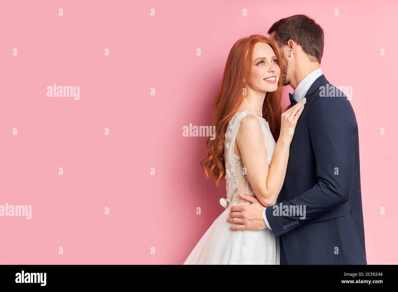 Attraktive Frau mit Auburn Haar umarmt ihren Verlobten in eleganten Anzug küssen sie. Glückliche junge Familie, Liebeskonzept Stockfoto