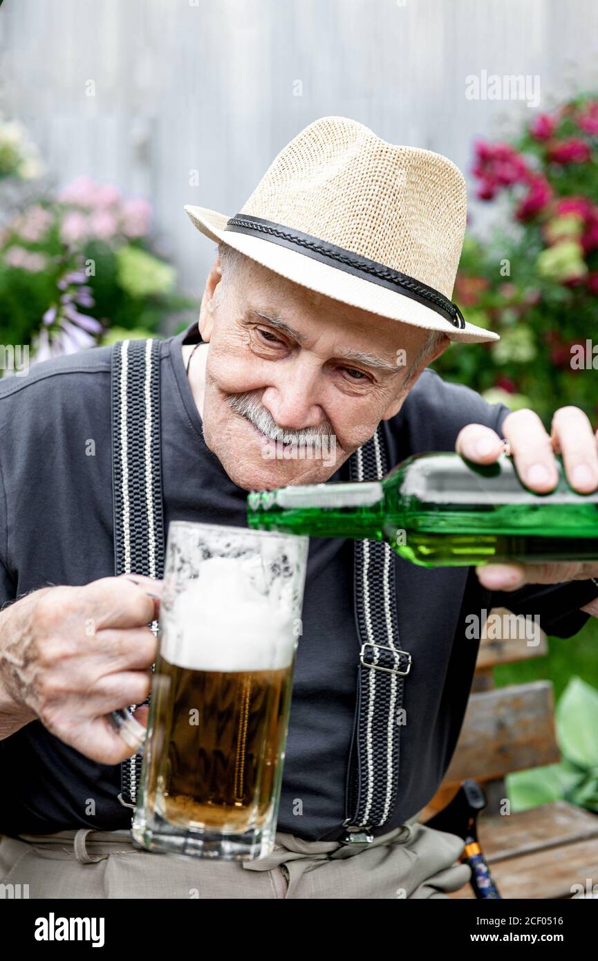 Älterer Mann in einem Hut trinkt Bier vor einer Kneipe auf einer Bank im  Garten. Der alte Mann gießt Bier in ein Glas. Nahaufnahme Stockfotografie -  Alamy
