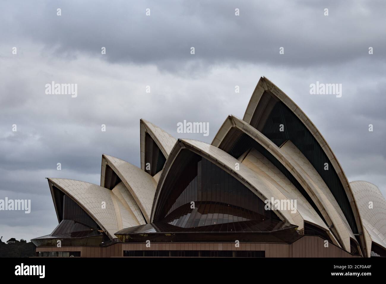 Die segelartige Architektur des Opernhauses von Sydney aus dem Hafen von Sydney. Hinter dem Opernhaus sind die Wolken stürmisch grau. Australien. Stockfoto