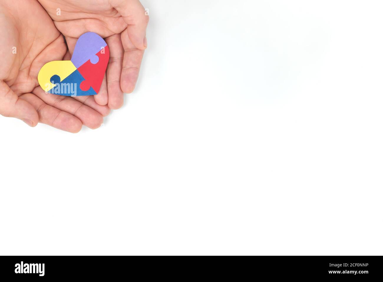 Cupped männliche Hände hält eine bunte Puzzle Herz Form Papier Ausschnitt. Draufsicht flach in weißem Hintergrund mit Kopierplatz. World Autism Awareness Day Konzept. Stockfoto