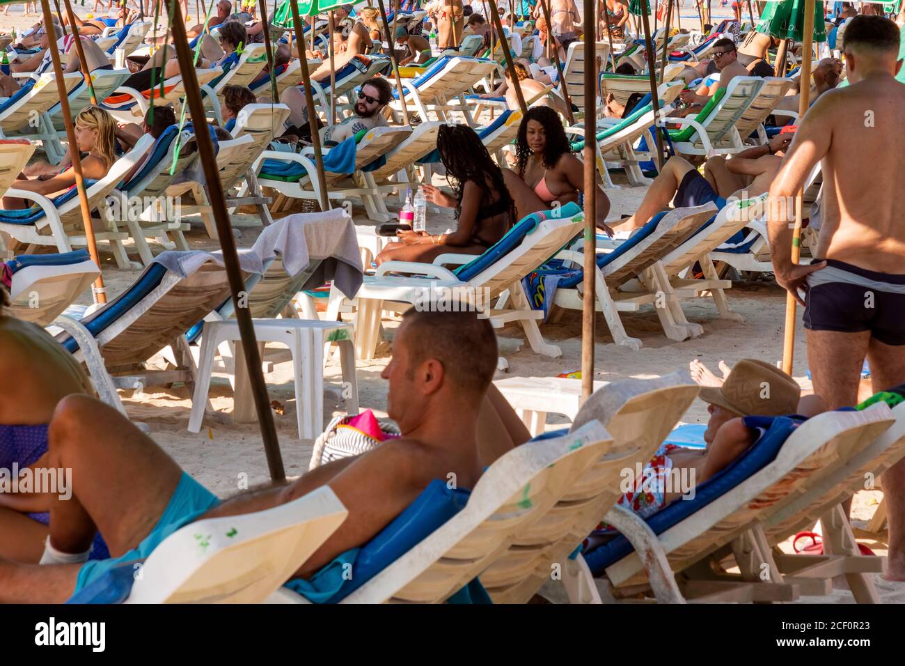 Touristen mit Sonnenschirmen und Liegestühlen am Strand von Patong, Phuket, Thailand Stockfoto