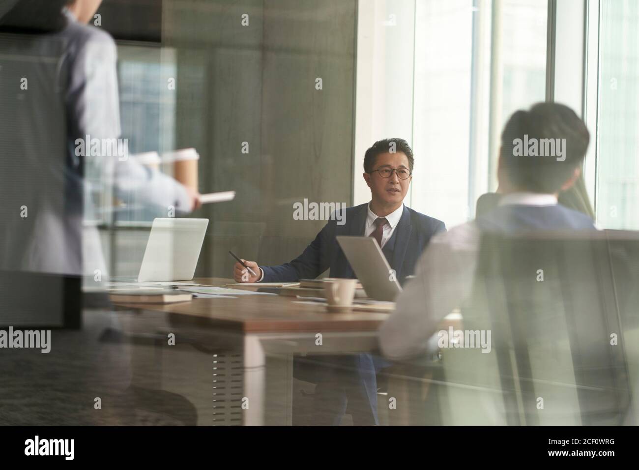 Durch-das-Glas-Schuss der Gruppe der asiatischen Geschäftsleute mit einem Diskussion im Tagungsraum Stockfoto