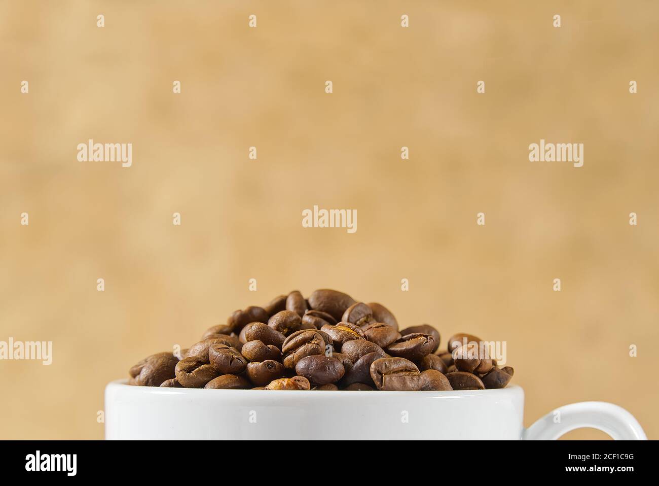 Internationaler Tag des Kaffees Konzept. Nahaufnahme weiße Kaffeetasse voller Kaffeebohnen auf beigem Hintergrund. Stockfoto