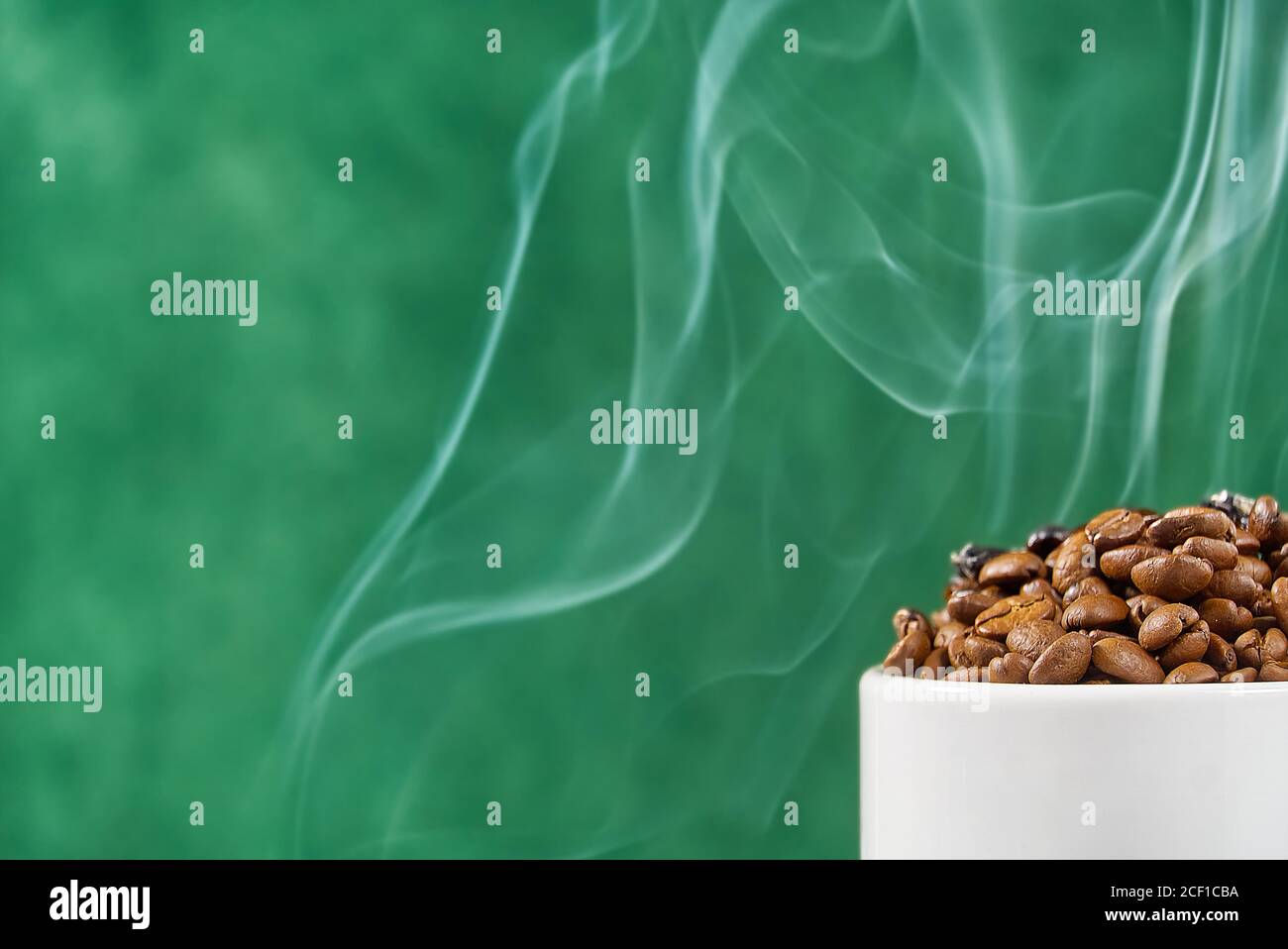Internationaler Tag des Kaffees Konzept. Nahaufnahme weiße Kaffeetasse voller Kaffeebohnen auf grünem Hintergrund mit Rauch auf der Oberseite. Stockfoto