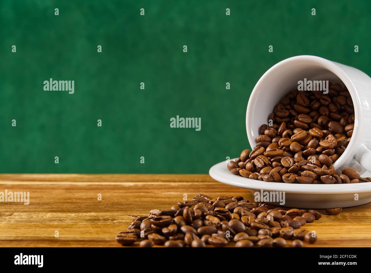 Internationaler Tag des Kaffees Konzept. Nahaufnahme weiße Kaffeetasse voller Kaffeebohnen auf dunkelgrünem Hintergrund. Stockfoto