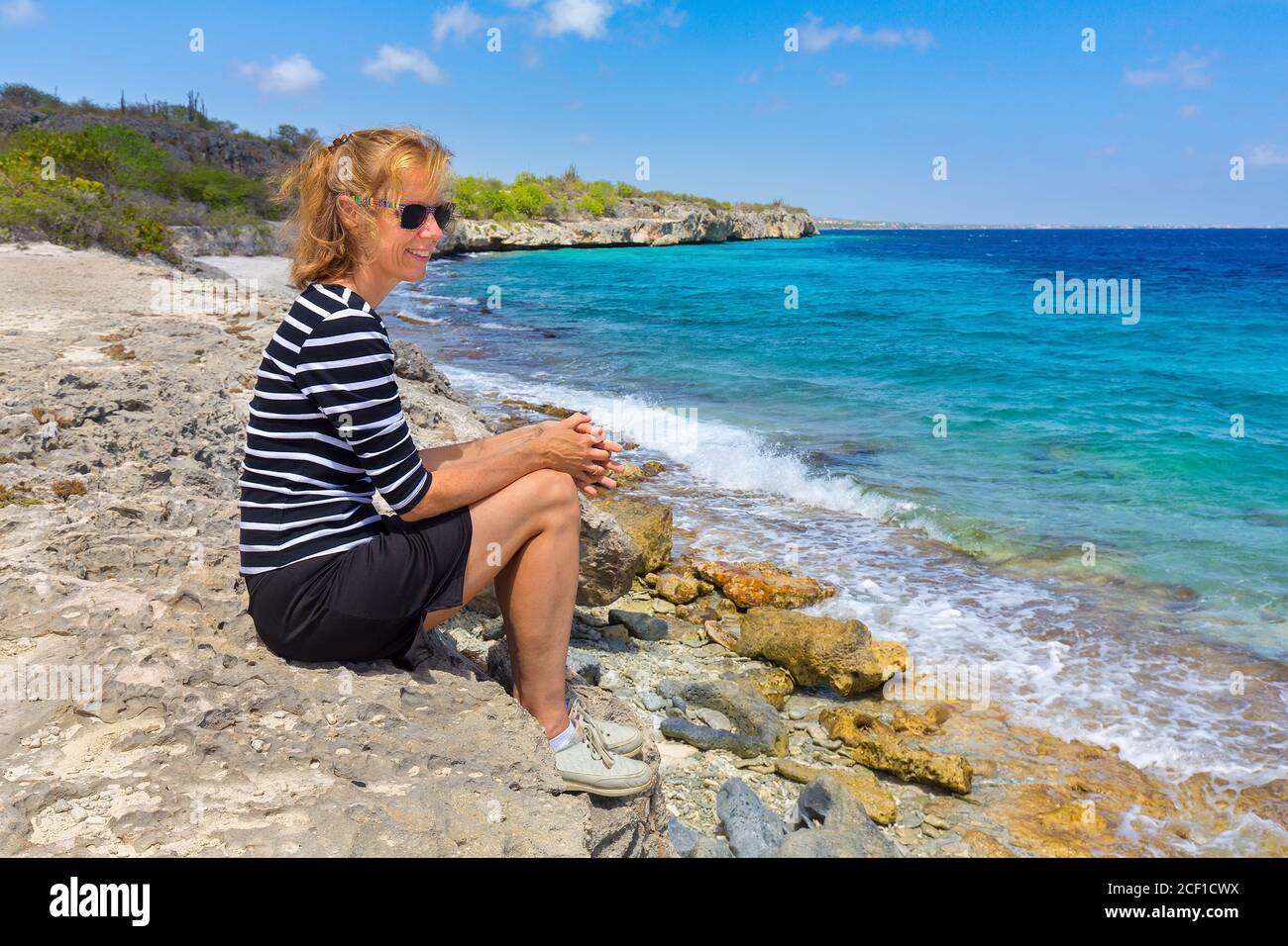 Kaukasische Frau mittleren Alters sitzt an der Küste der Niederländischen Antillen Stockfoto