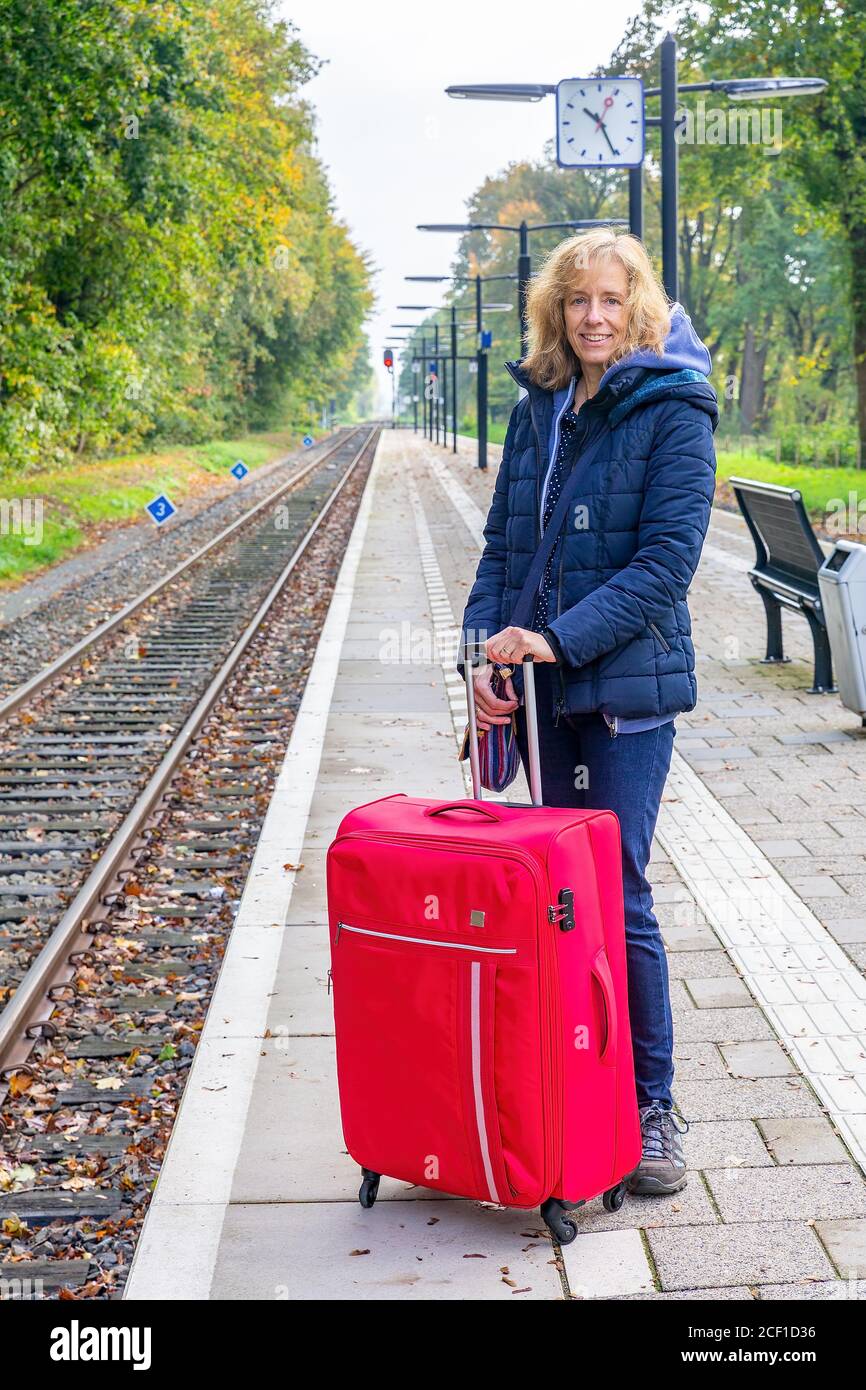 Kaukasische Frau mit rotem Koffer wartet auf holländischen Bahnhof Stockfoto