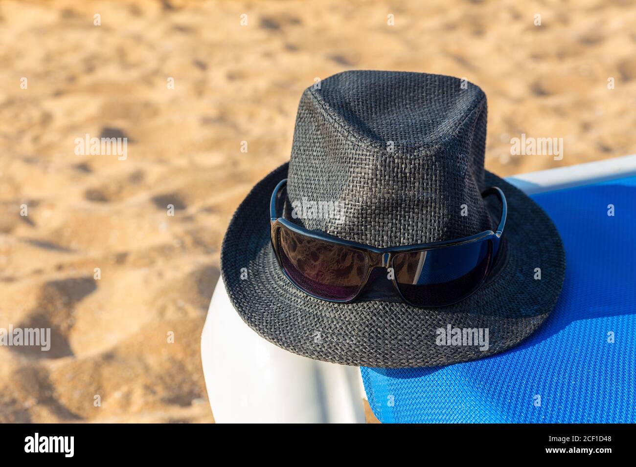 Grauer Sonnenhut und Sonnenbrille auf blauem Strandbett Küste Stockfoto