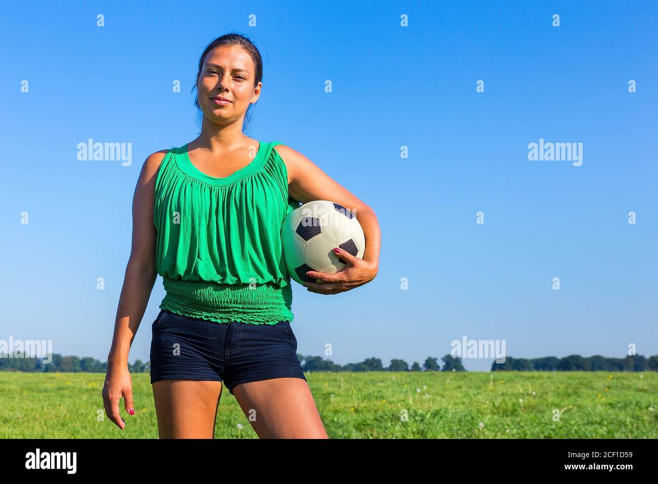 Stehende junge kolumbianische Frau hält Fußball vor Blau Himmel Stockfoto