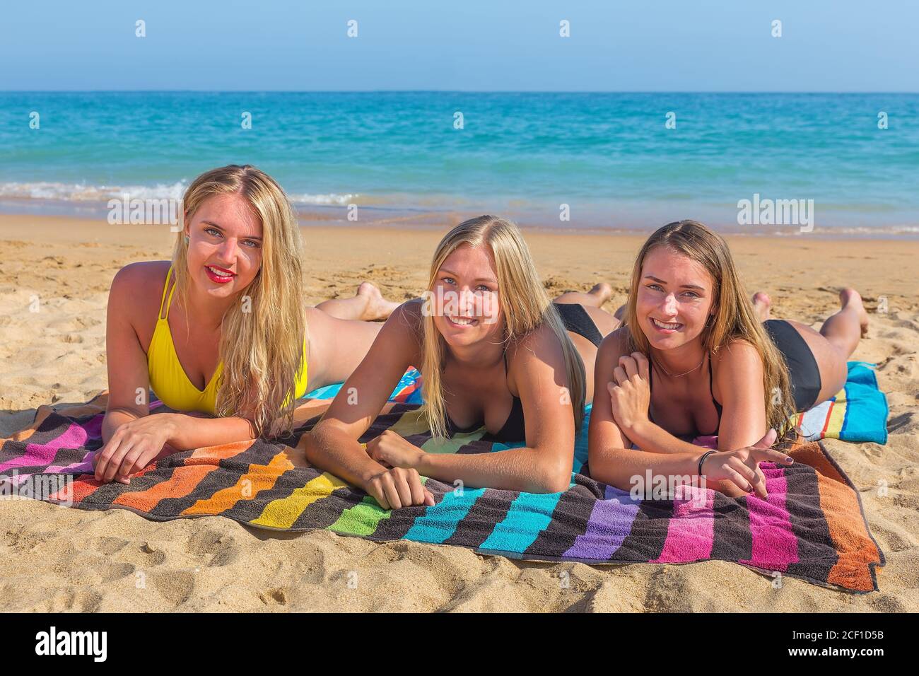 Drei hübsche kaukasische Mädchen liegen am Strand und sonnen sich an der Küste Mit blauem Meer Stockfoto