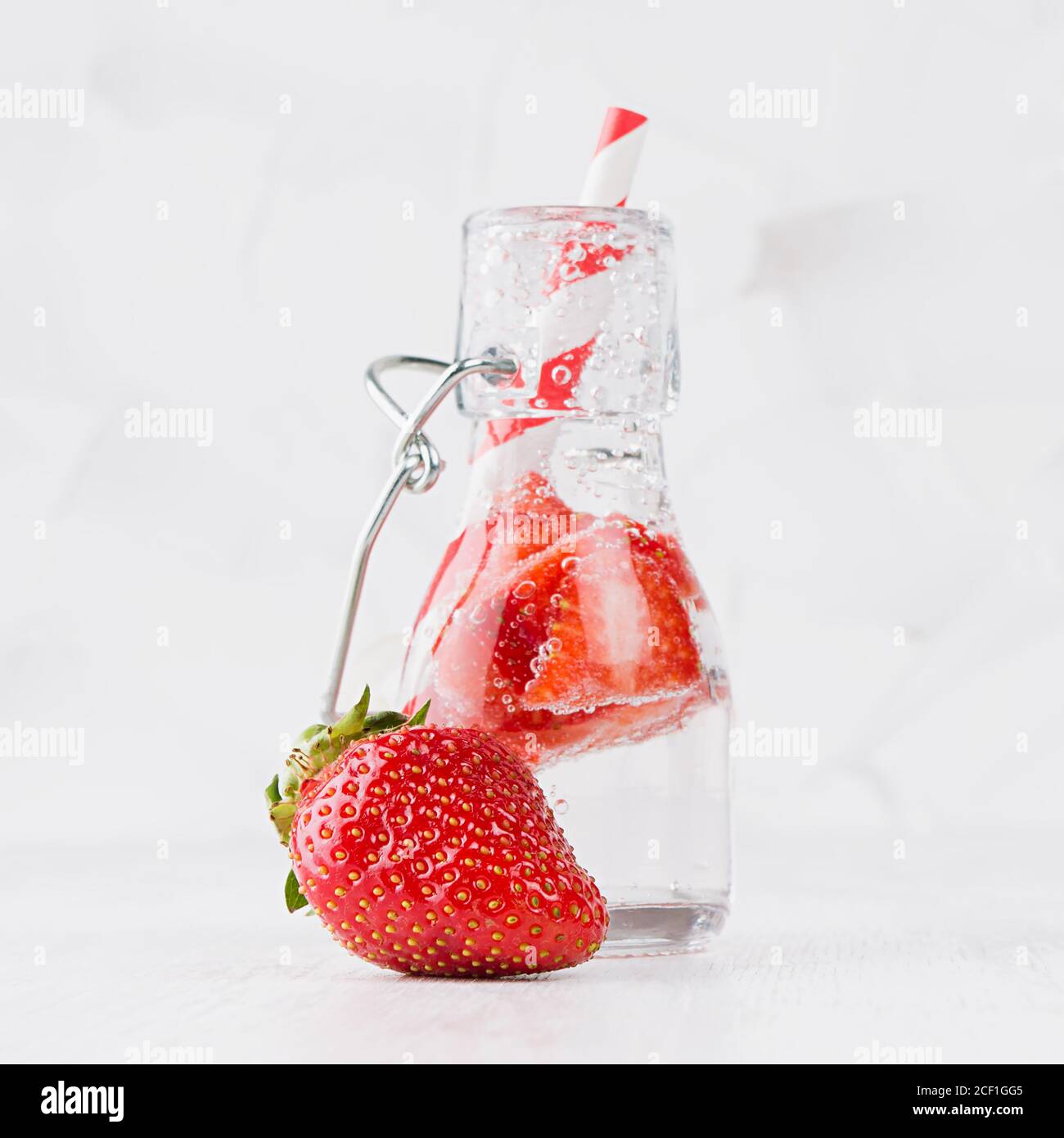 Frischer Sommercocktail mit reifen Erdbeeren, Soda, Stroh in Yoke Flasche auf eleganten weichen hellen weißen Holzbrett und Gipswand, quadratisch. Stockfoto