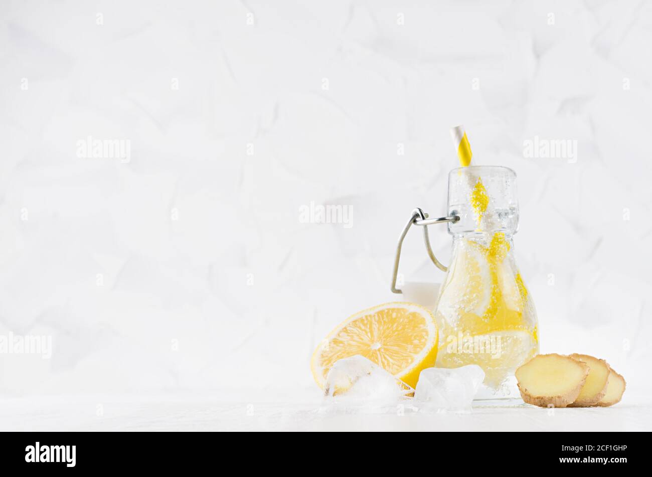 Erfrischendes kaltes Fruchtgetränk mit Zitruszitrone, hellen Blasen, Eis, Ingwer und Stroh in transparenter Yoke-Flasche im eleganten weißen Interieur auf Holztabl Stockfoto