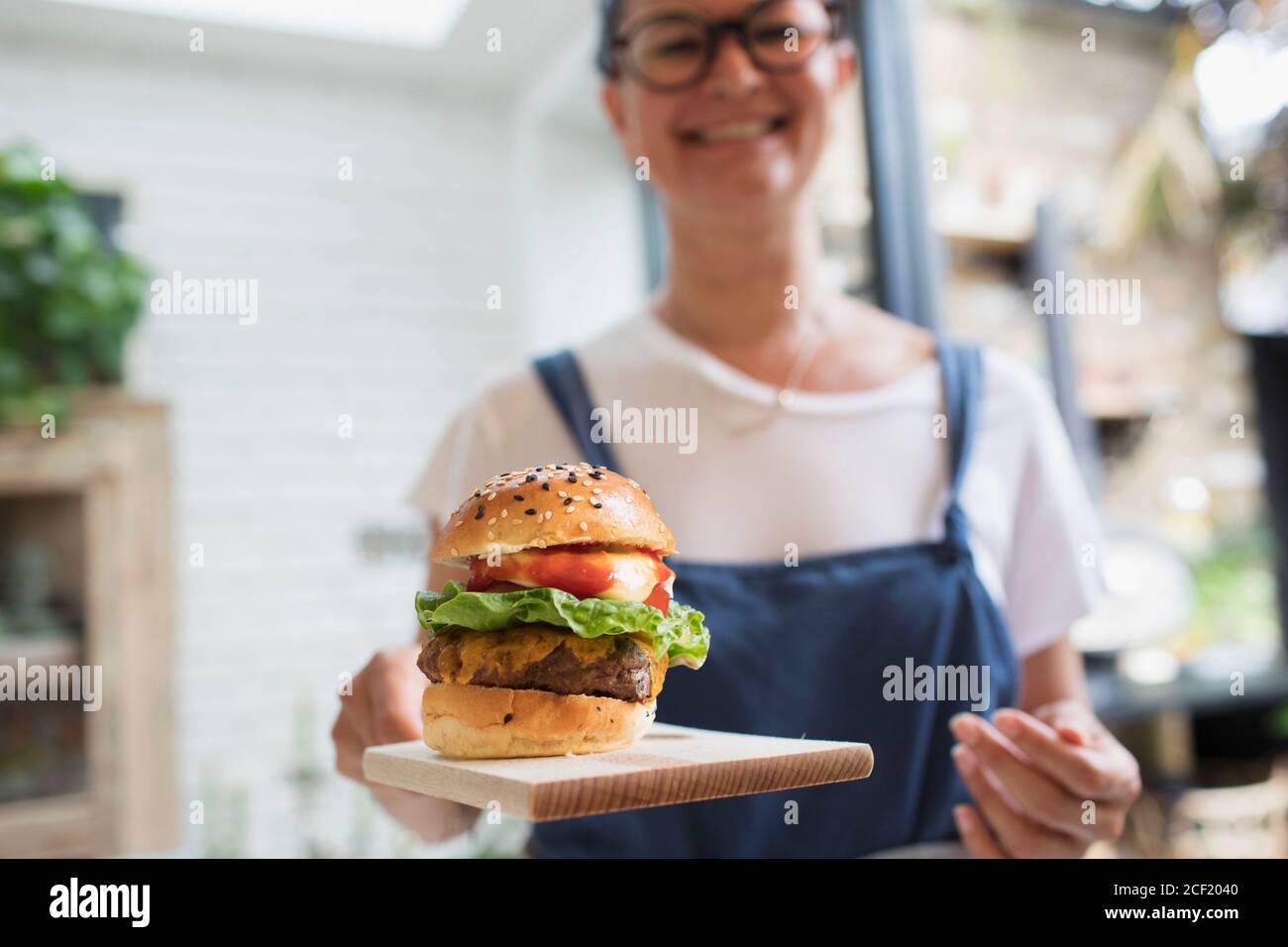 Portrait lächelnde Frau mit Cheeseburger auf Schneidebrett Stockfoto