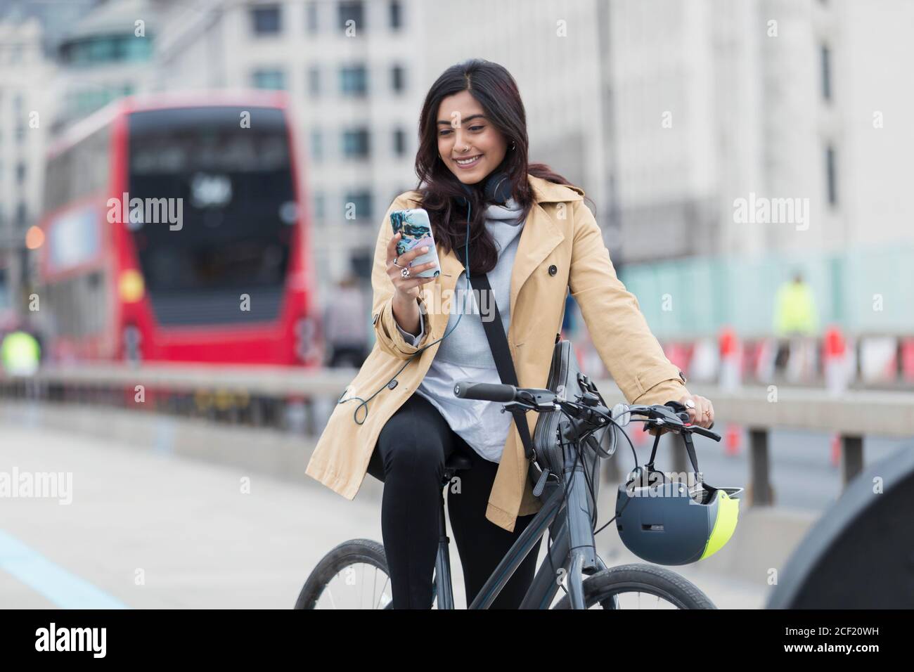 Lächelnde Geschäftsfrau mit Smartphone auf dem Fahrrad in der Stadt, London, Großbritannien Stockfoto