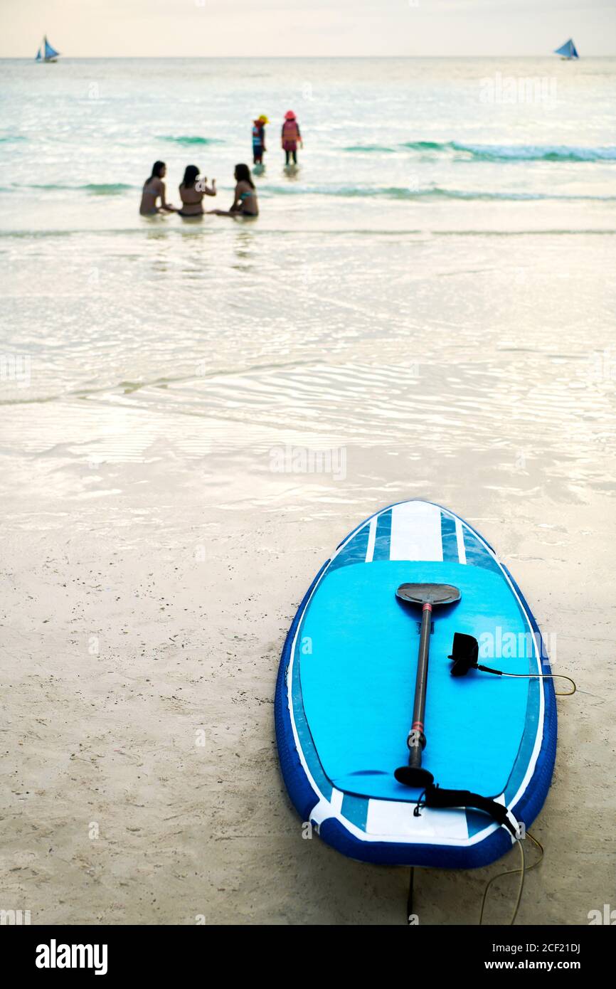 Junge Menschen genießen die Küste entlang des White Beach auf Boracay Island, Philippinen. Ein blaues Paddle Board kann am Sandstrand gemietet werden. Stockfoto