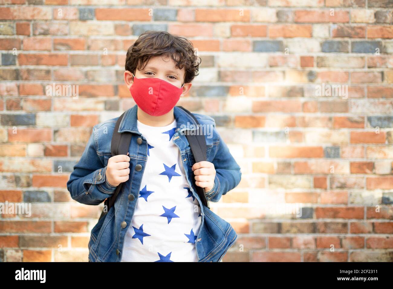 Kaukasisches Kind mit Schultasche zu Fuß auf der Straße. Er trägt eine Gesichtsmaske. Zurück in die Schule nach covid-19 Quarantäne und Sperrung. Stockfoto