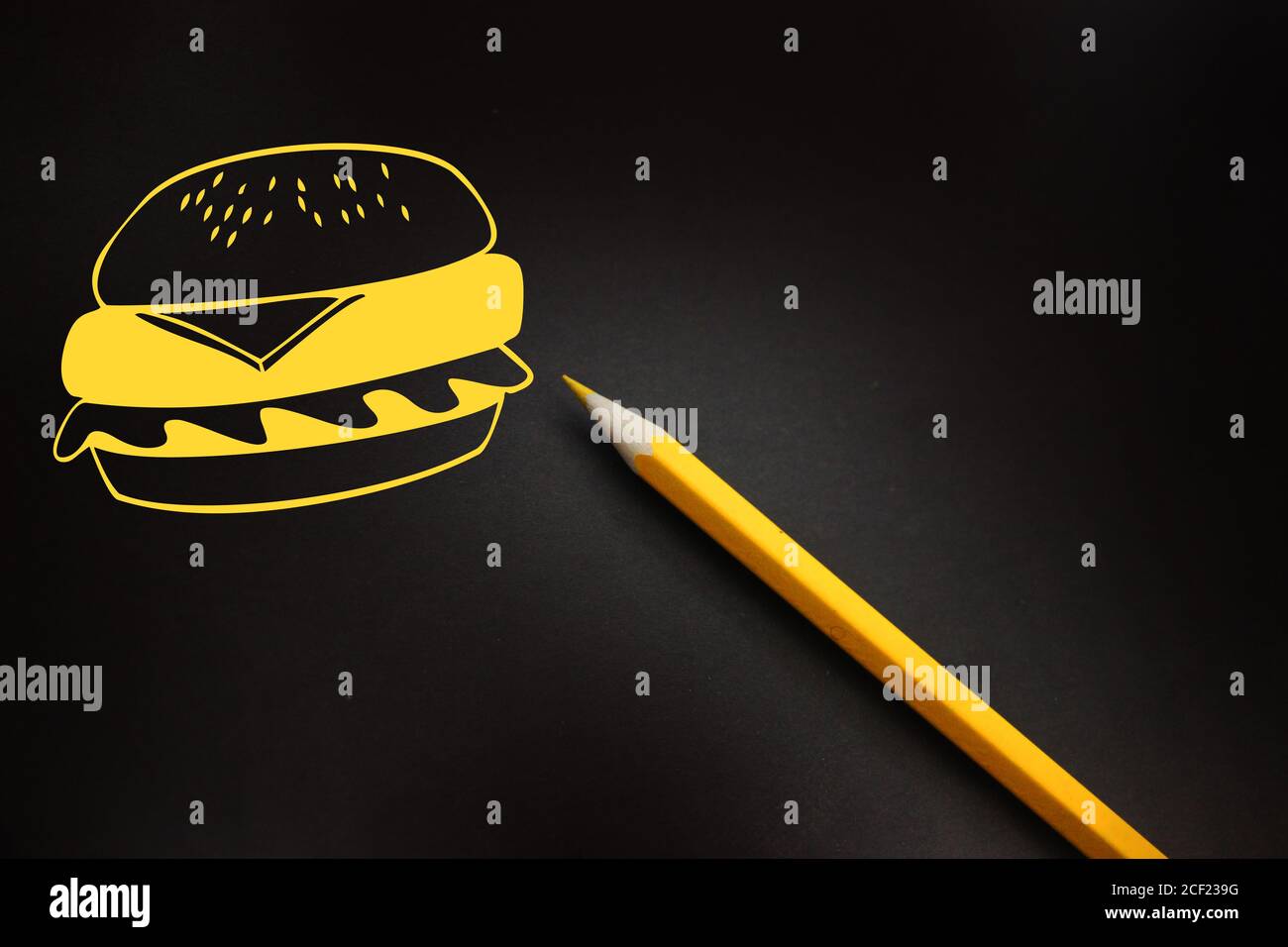 Hamburger Icon-ähnliche Zeichnung in gelbem Fast Food auf schwarzem Brett mit gelbem Bleistift dazu. Fatfood ungesunde Ernährung Konzept Stockfoto