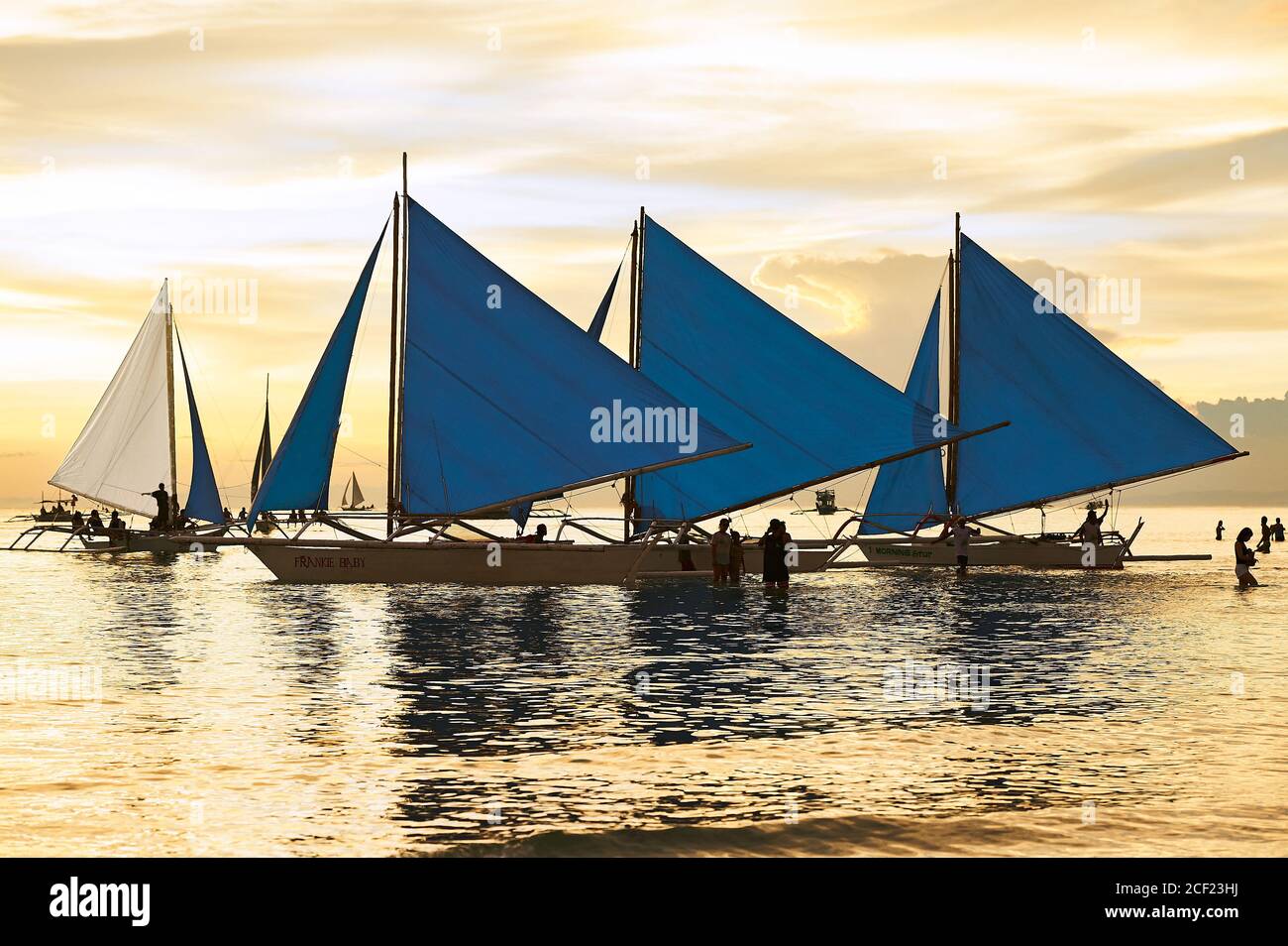 Blaue Segelboote warten auf Touristen an der Küste am White Beach auf Boracay Island, Philippinen mit einem goldenen Sonnenuntergang in den Himmel und Wasser Stockfoto