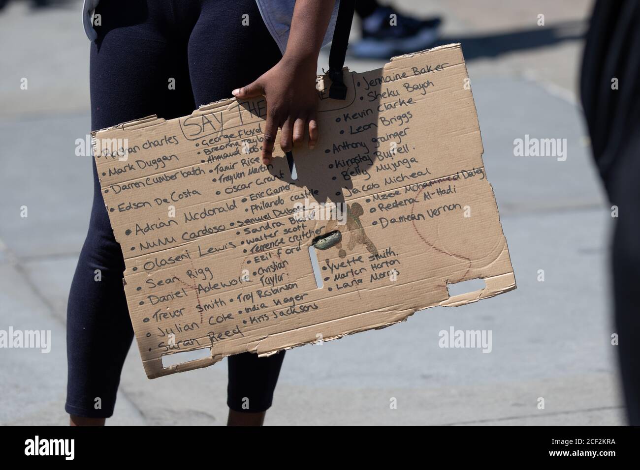 Ein Protestor, der ein Schild mit den Namen vieler schwarzer Menschen trägt, die durch die Polizei in den USA und Großbritannien in Black Lives Matter London getötet wurden Stockfoto