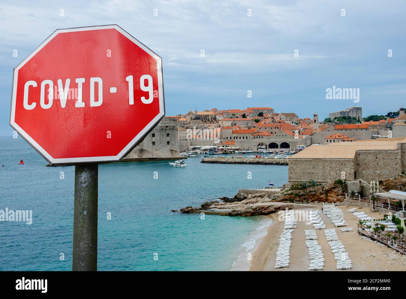 COVID-19 Zeichen gegen Blick auf Mauern und Strand in Dubrovnik, Kroatien. Warnung vor Pandemie in Kroatien. Coronavirus-Krankheit. COVID-2019-Warnzeichen Stockfoto