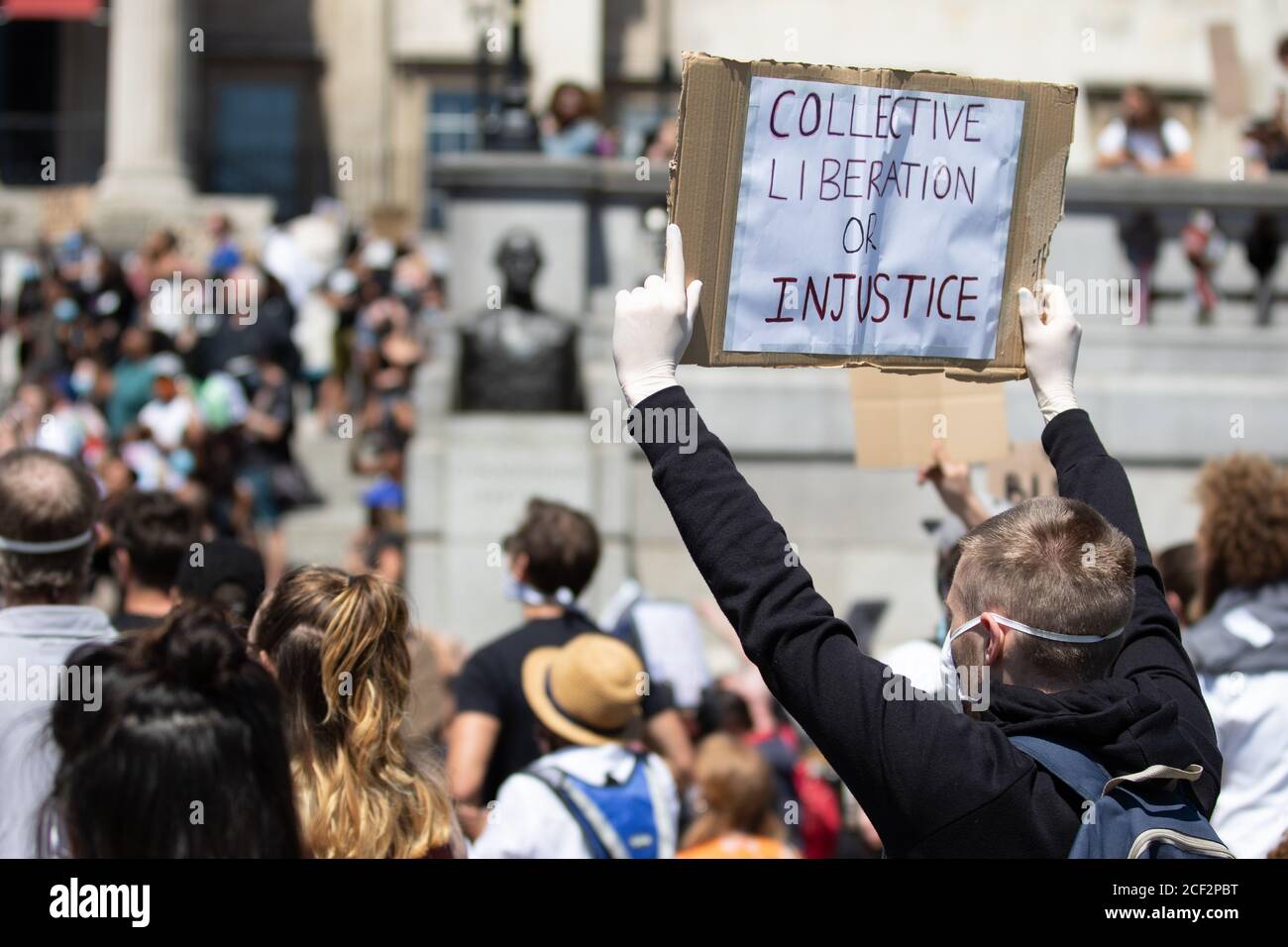 Ein weißer, männlicher Protestant hält ein Schild mit der Aufschrift "Collective Liberation or Injustice" bei einem Protest von Black Lives Matter auf dem Trafalgar Square in London Stockfoto