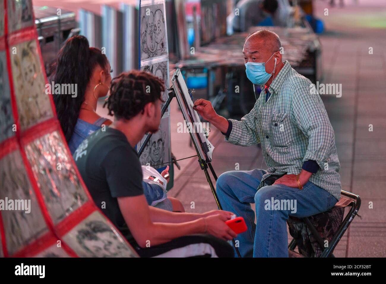 Ein Sketch-Künstler trägt eine Schutzmaske, als er am 1. September 2020 in New York ein Porträt auf dem Times Square erstellt. Stockfoto