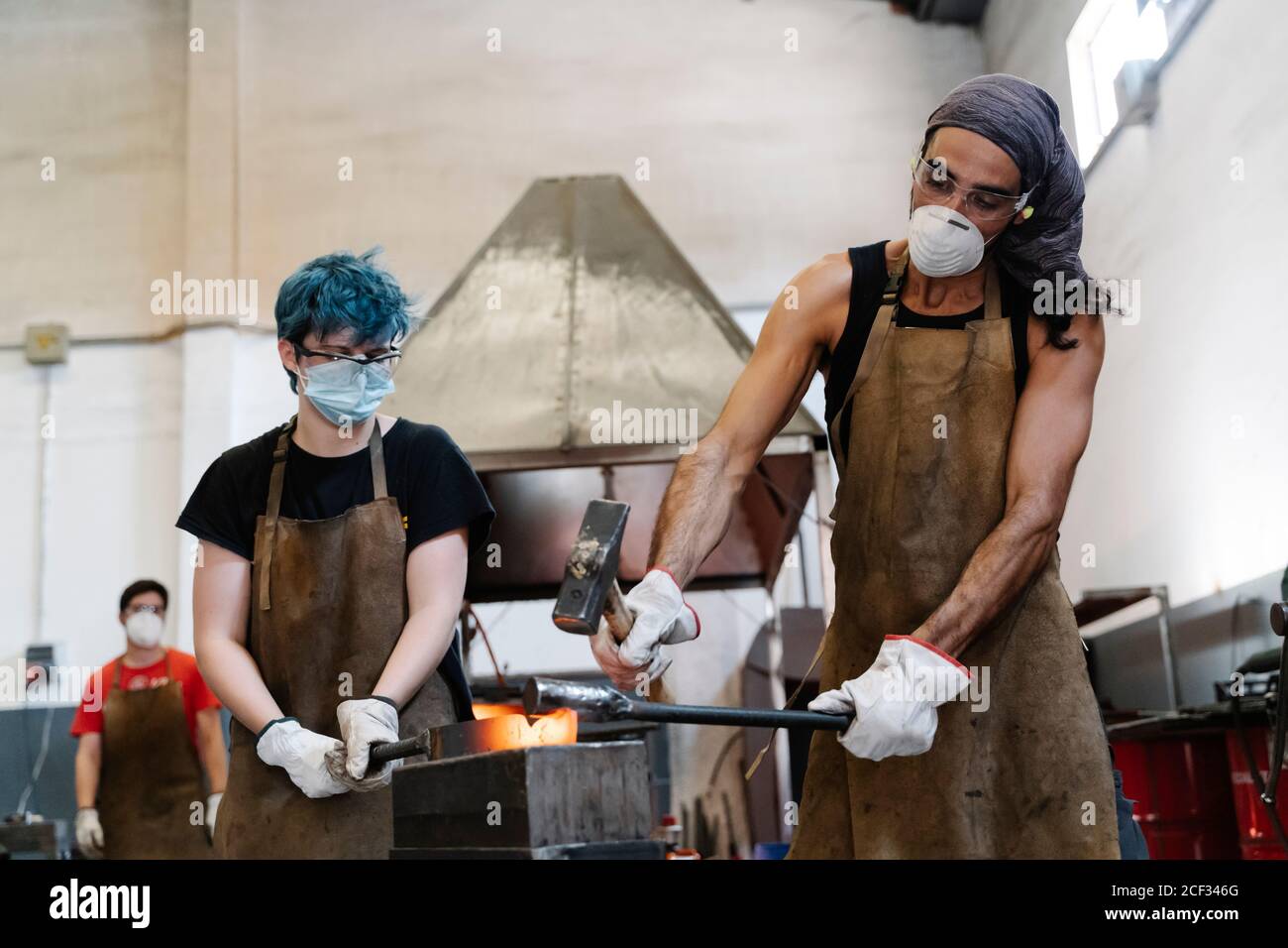 Schmiede in Masken schlagen heißes Metall mit Hammer während der Arbeit Stockfoto