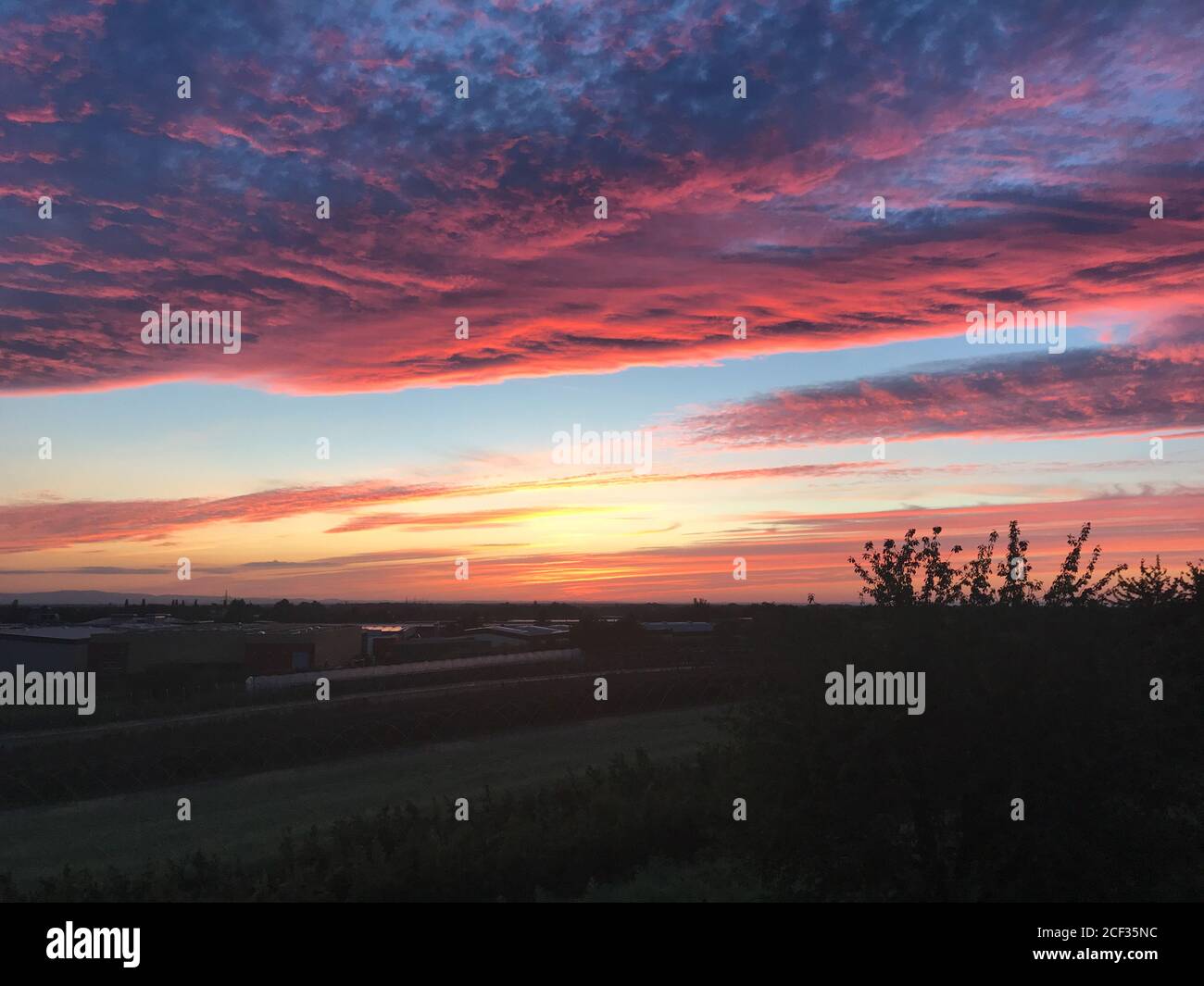 Blick über ländliche Gebäude von einem bunten Sonnenuntergang mit rosa Wolkenformationen und ein orangefarbenes Leuchten über dem Horizont Stockfoto