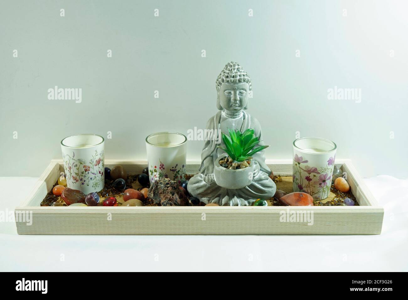 Kleine buddha-Figur mit Pflanze, drei Kerzen und einigen Steinen. Ruhe. Weißer Hintergrund Stockfoto