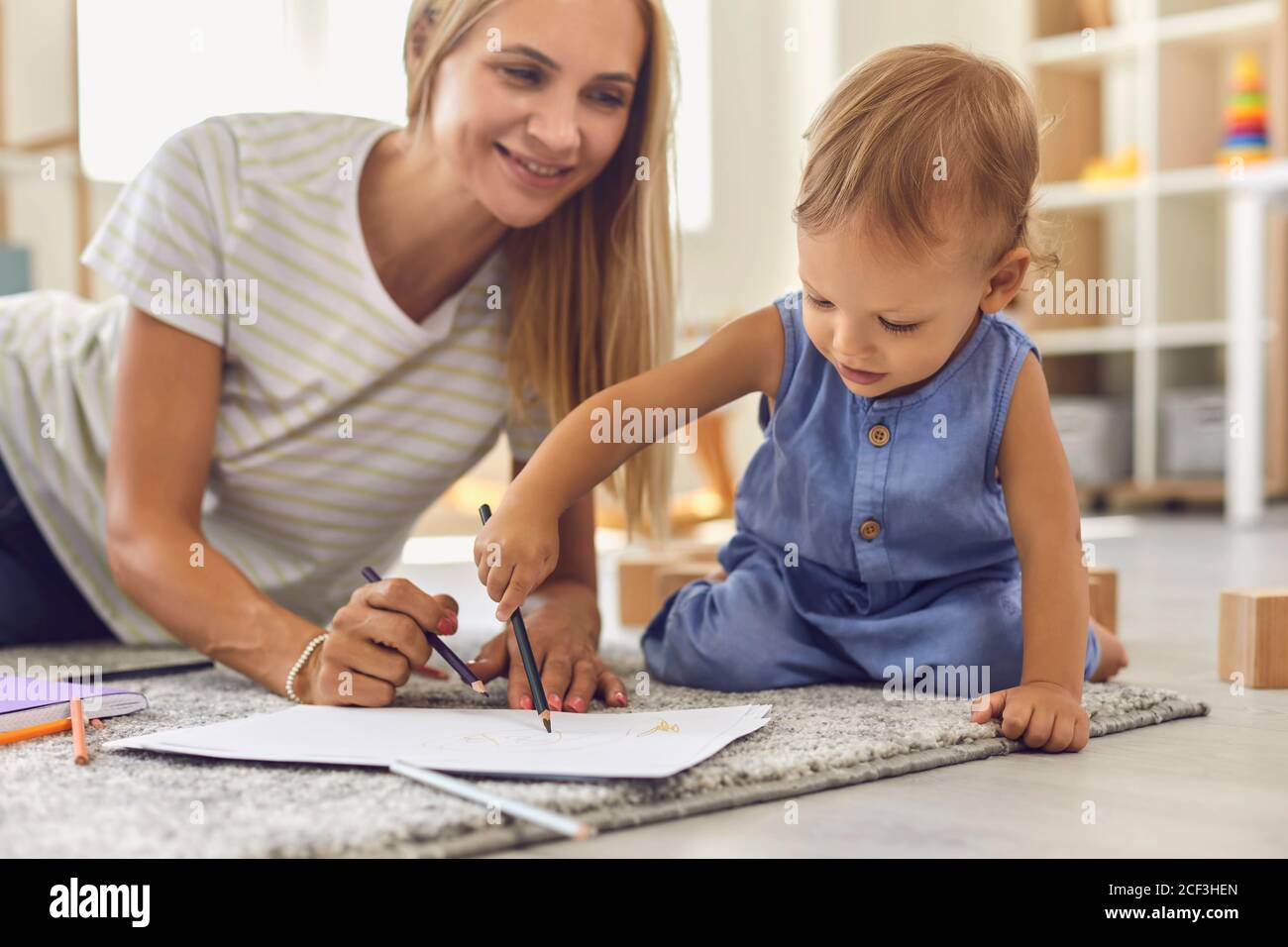 Liebenswert Kleinkind Kritzelei auf Papier mit Bleistift, während sitzend auf Boden mit seinem jungen Kindermädchen Stockfoto