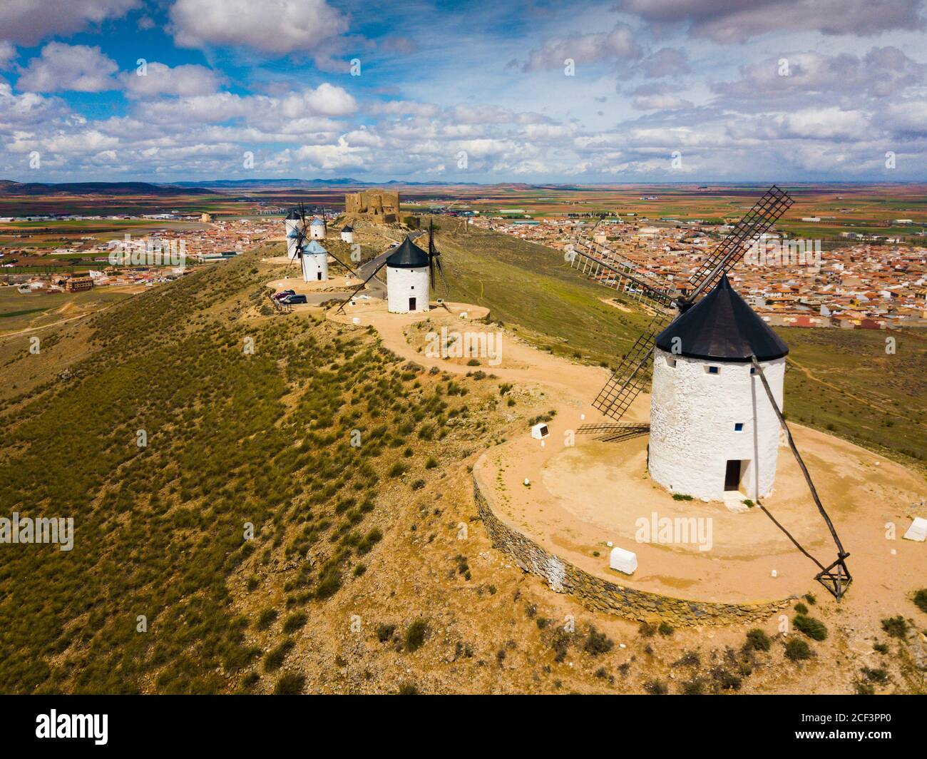 Luftbild des Weißen zylindrischen Türmen und spitzen Dächern der alten spanischen Windmühlen auf Hintergrund mit Consuegra Stadtbild Stockfoto