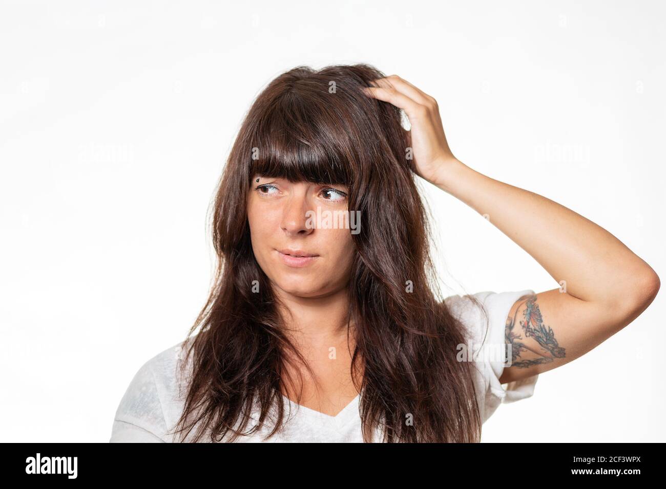 Porträt einer Frau mit einem Tattoo auf ihrem Arm, das sich hinter ihrem Kopf befindet und an Migräne leidet. Weißer Hintergrund. Das Konzept der Kopfschmerzen. Stockfoto