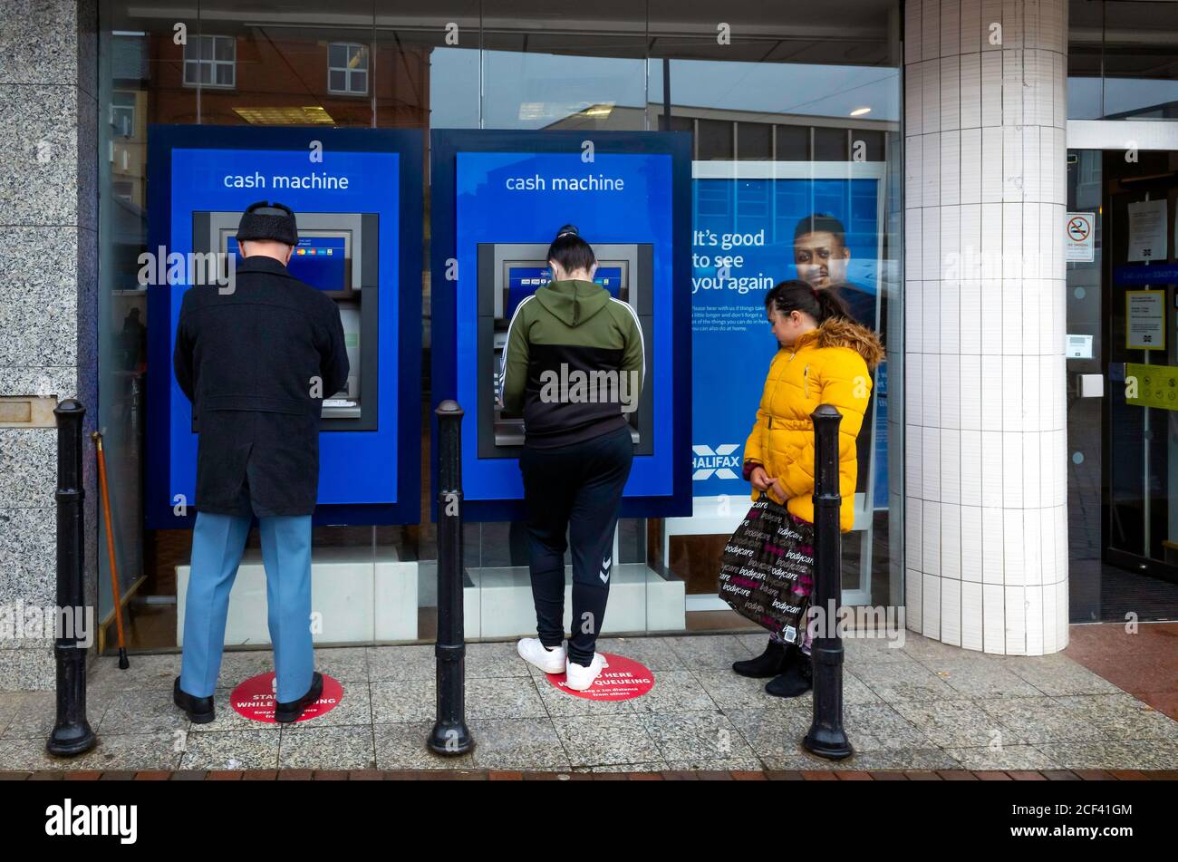 Ein Mann und eine Frau ziehen nebeneinander Bargeld ab Von einer Halifax Bank Geldautomat oder Geldautomat während ein Mädchen schaut auf Stockfoto