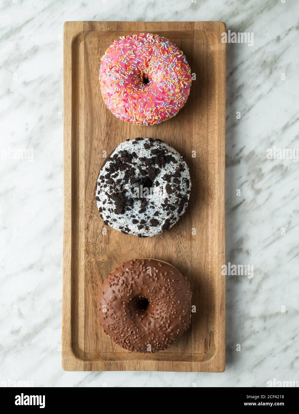 Draufsicht auf traditionelle süße Donuts mit Glasur auf gelegt Holzbrett auf heller Marmoroberfläche Stockfoto