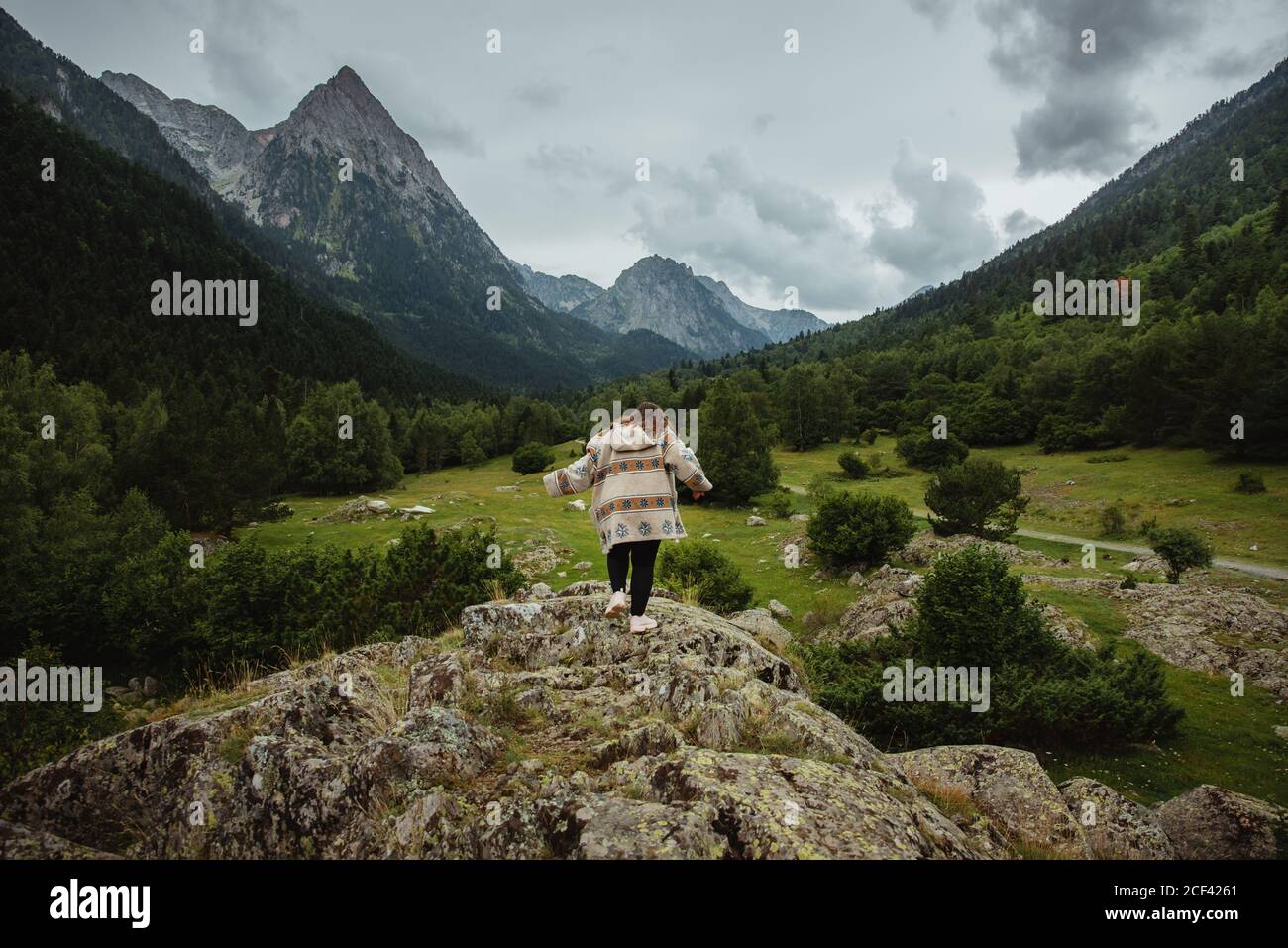 Rückansicht einer unkenntlichen Frau in lässigem Outfit, die am bewölkten Tag im majestätischen Tal auf einem rauen felsigen Hügel läuft Stockfoto