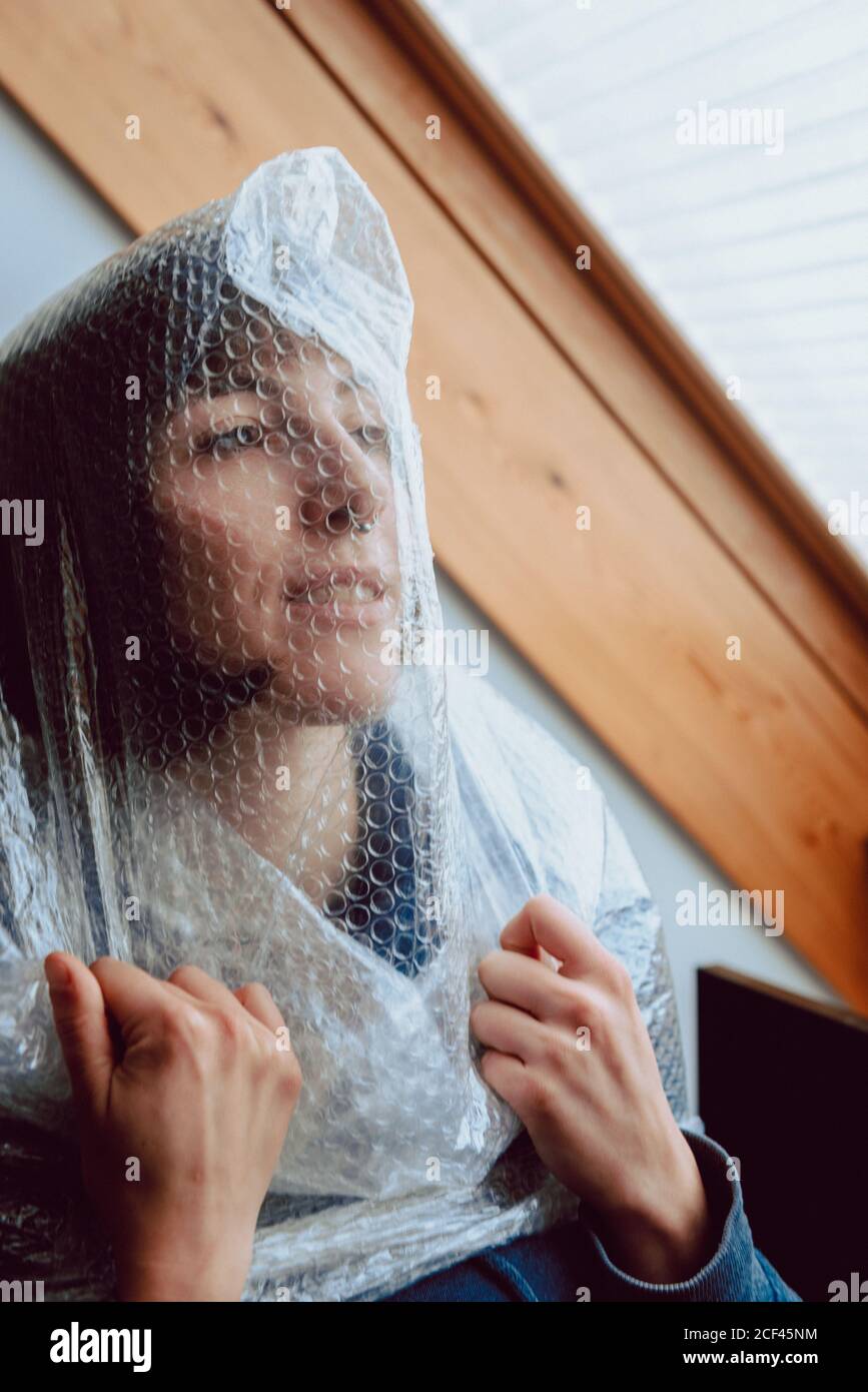 Verängstigte Frau, die versucht, sich selbst zu befreien, während sie in Luftpolsterfolie verwickelt ist Stockfoto