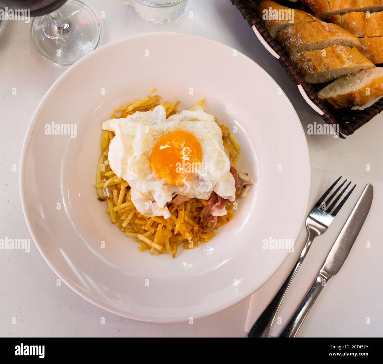 Traditionelles, appetitliches spanisches Mittagessen - Spiegelei mit pommes frites Und Scheiben von Jamon auf weißem Teller Stockfoto