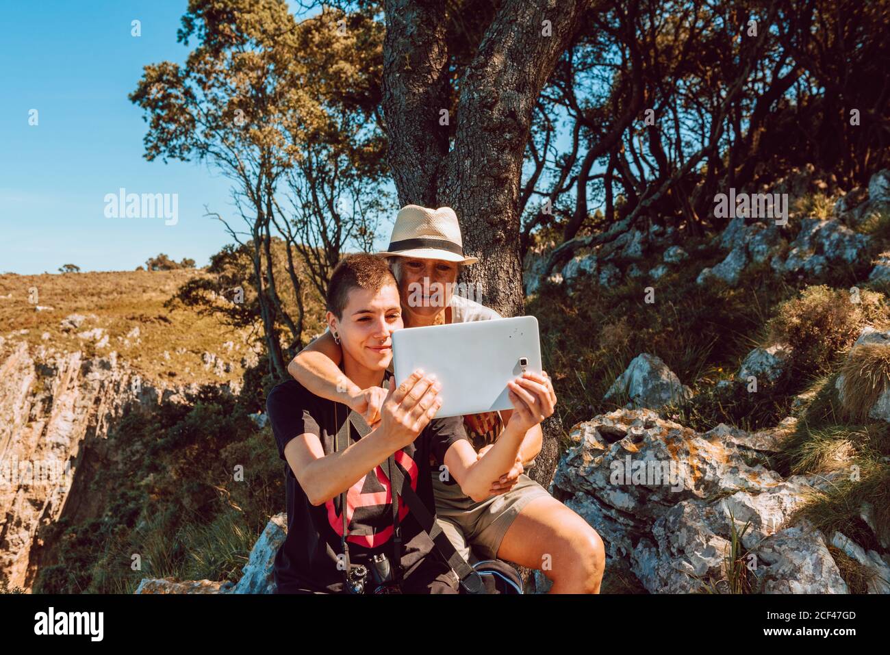 Fröhliche Großmutter und Enkelin sitzen auf Steinen und beobachten Tablette Stockfoto