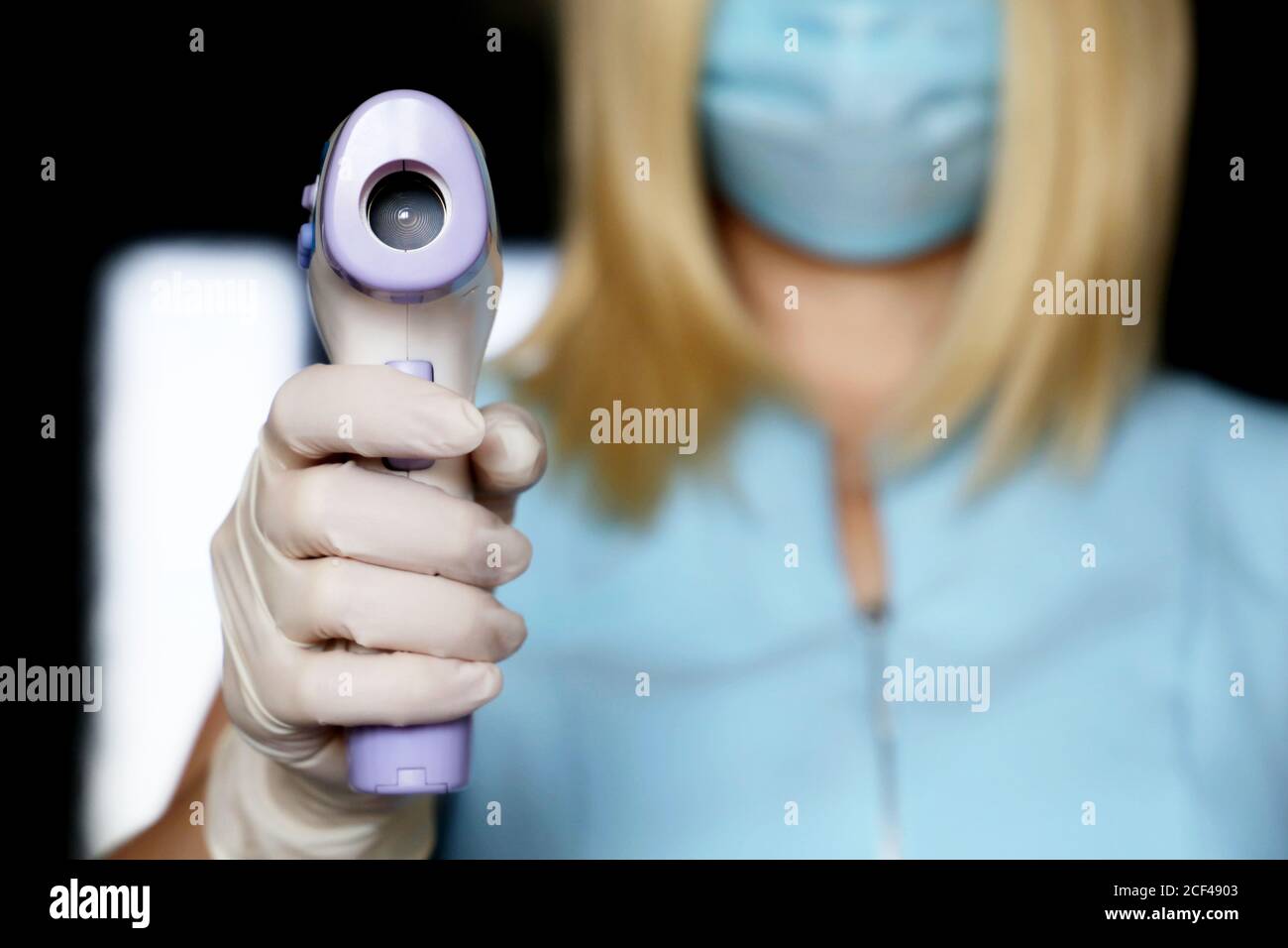 Coronavirus Symptome, Frau in medizinischen Gesichtsmaske misst Körpertemperatur. Ärztin mit einem digitalen isometrischen berührungslosen Thermometer in den Händen Stockfoto