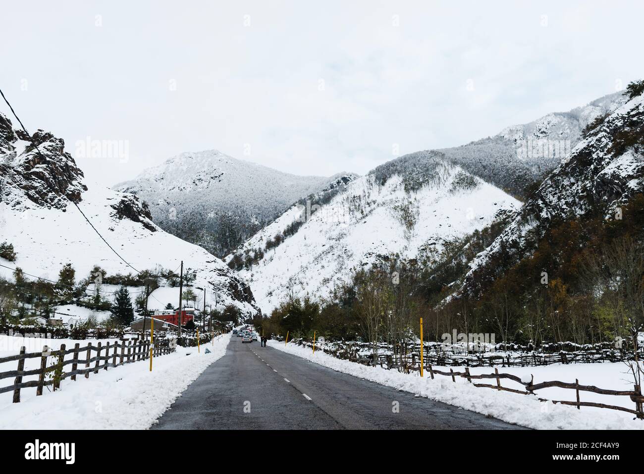 Asphaltierte Straße zwischen verschneiten Bergen und Wäldern mit kleinen Holz Zäune des Dorfes an den Seiten im Winter tagsüber Stockfoto
