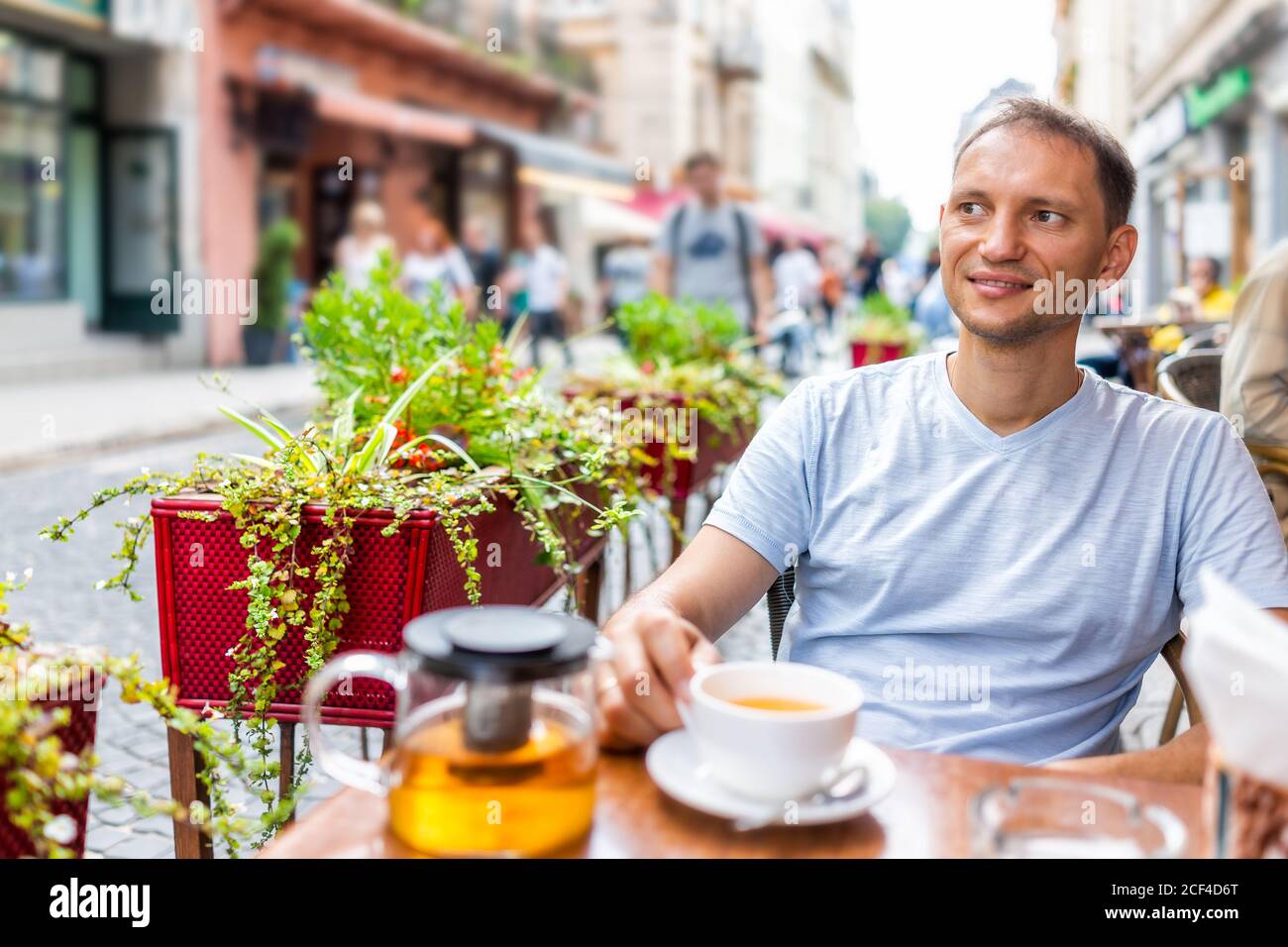 Junger glücklicher lächelnder Mann sitzt im europäischen Café-Restaurant mit Blick auf die Menschen beobachten im Sommer in Lviv oder Lvov, Ukraine Stadt am Tisch Stockfoto