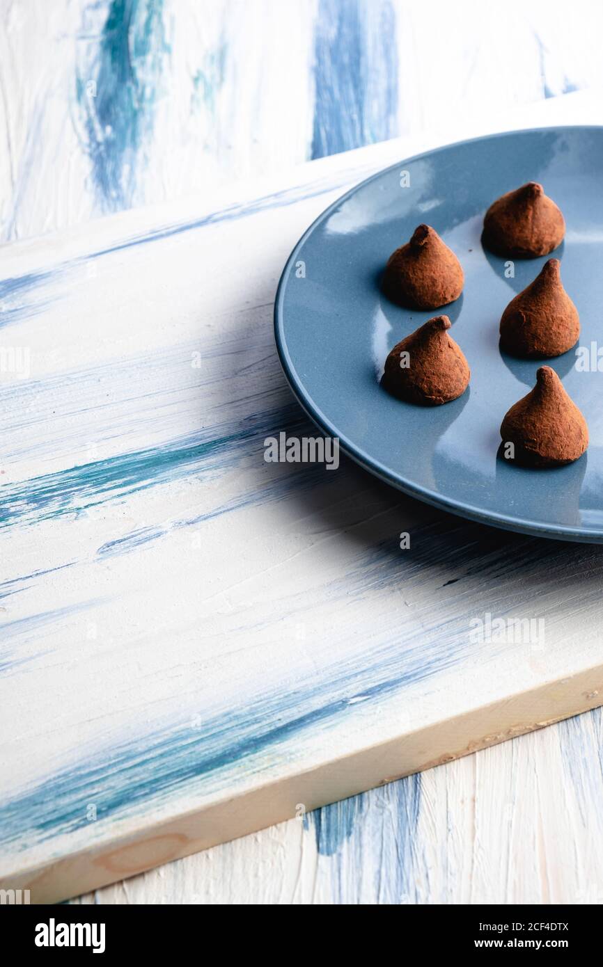 Von oben halbblauer Teller mit hausgemachter kegelförmiger Schokolade Süßigkeiten auf Holz rustikalen Tisch Stockfoto