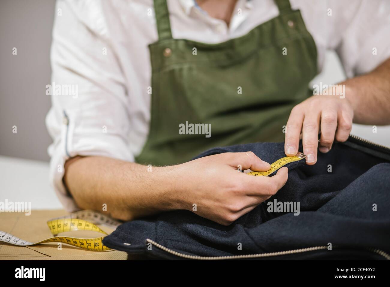 Nicht erkennbare männliche Näherin mit Maßband bei der Überprüfung der genauen Größe Von Mustern, während die Herstellung maßgeschneidertes Outfit für Kunden in modernen atelier Stockfoto