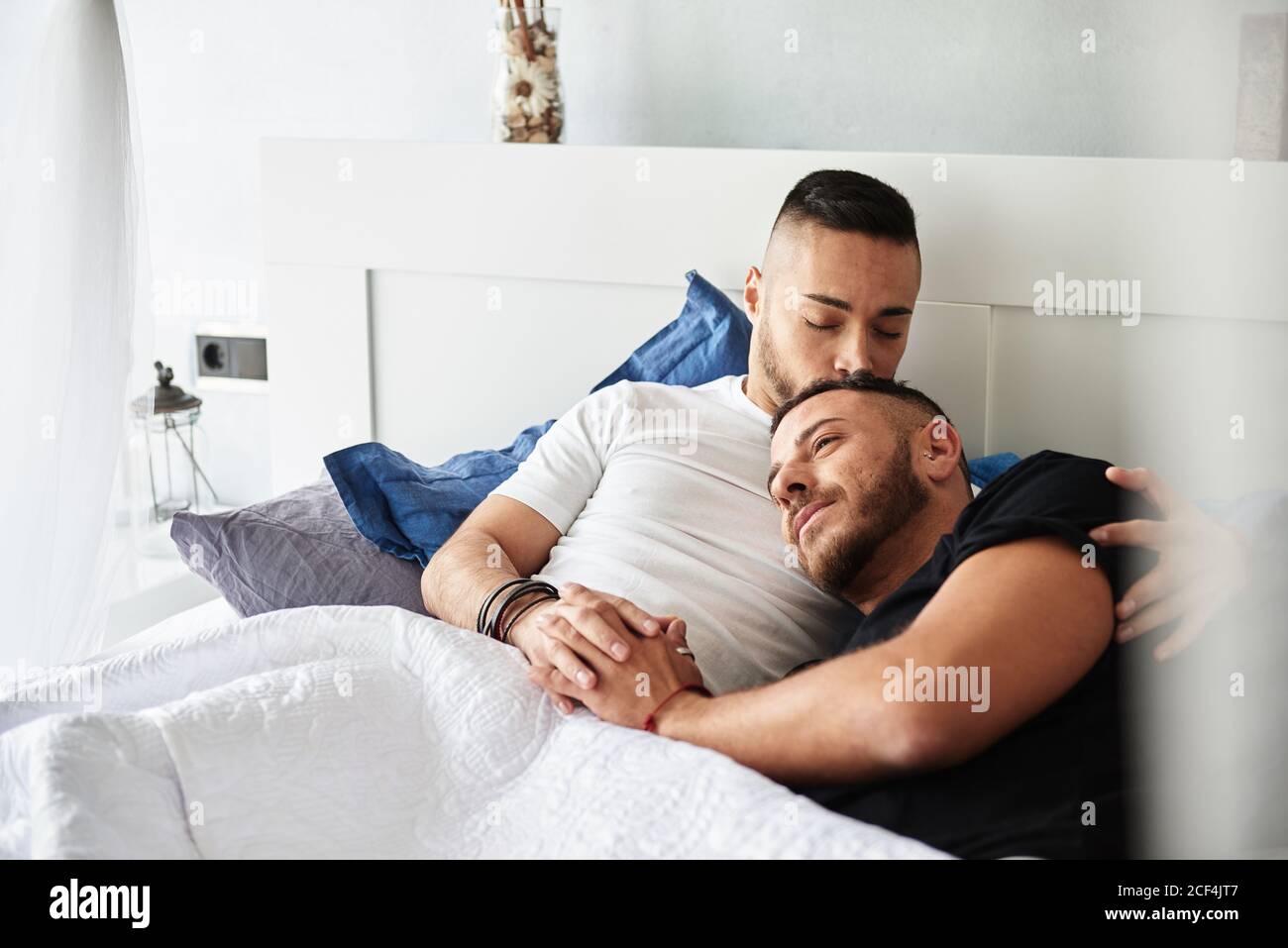 Fröhliche homosexuelle Männer liegen auf dem Bett, halten Hände mit ineinandergreifenden Fingern