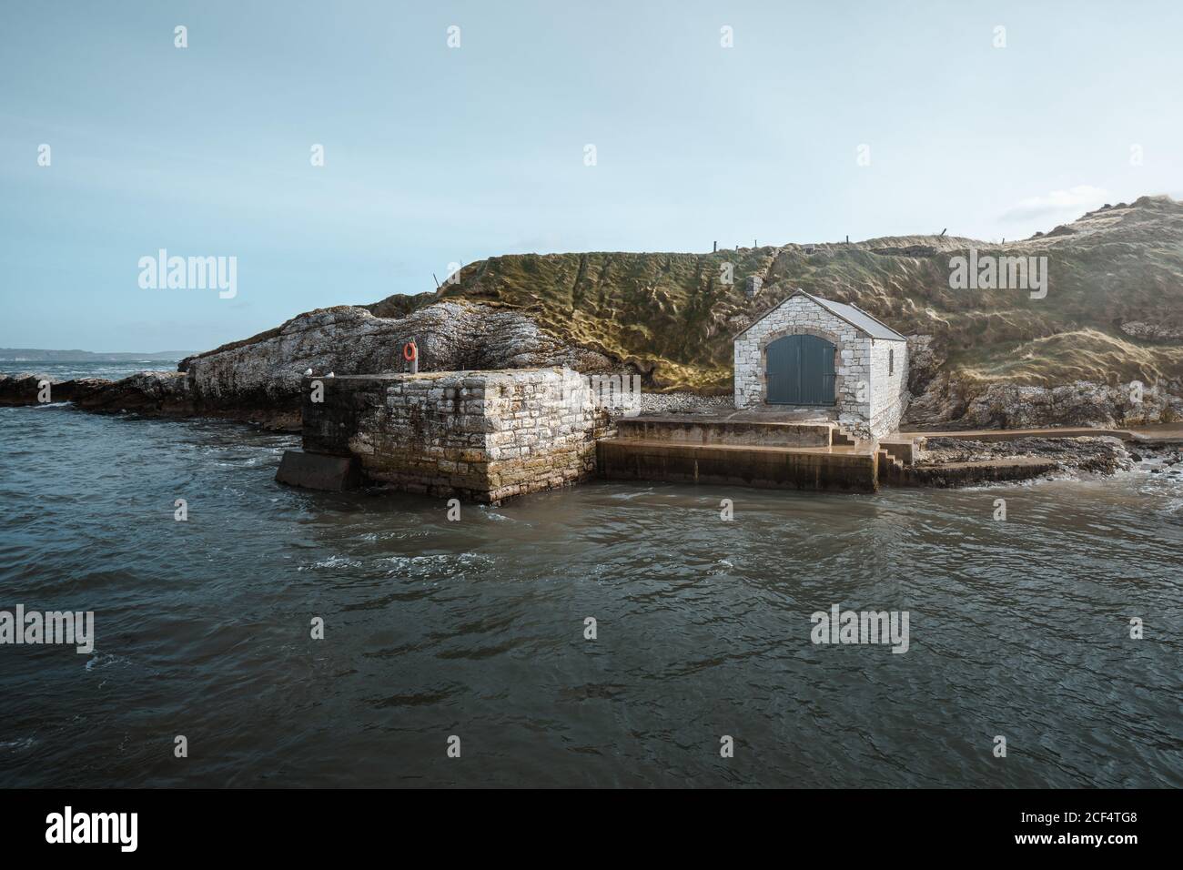 Antikes Steingebäude mit Türen am malerischen Pier von Ballintoy Hafen auf Felsen Hintergrund Stockfoto